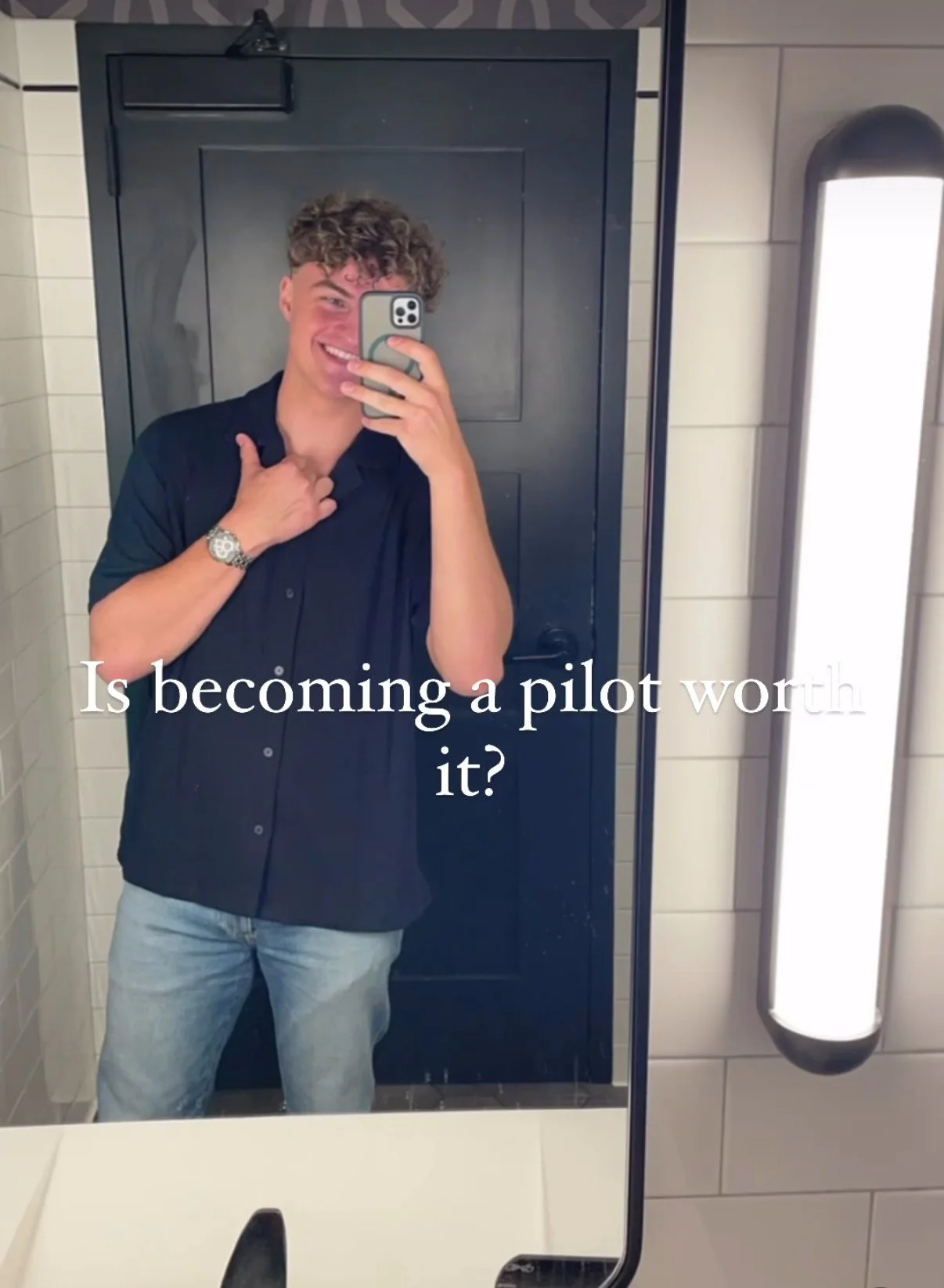 Person taking a selfie in a bathroom mirror, wearing a black shirt and jeans, with the text 'Is becoming a pilot worth it?' overlayed on the image.
