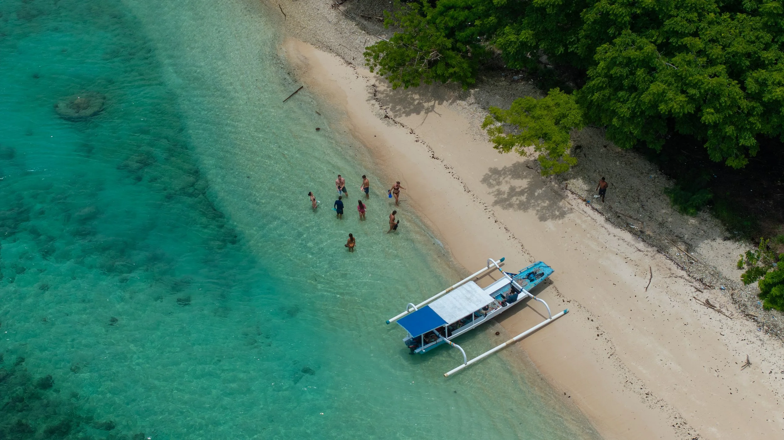 Aerial view of a quiet beach at Gili Rengit with guests and a traditional outrigger boat