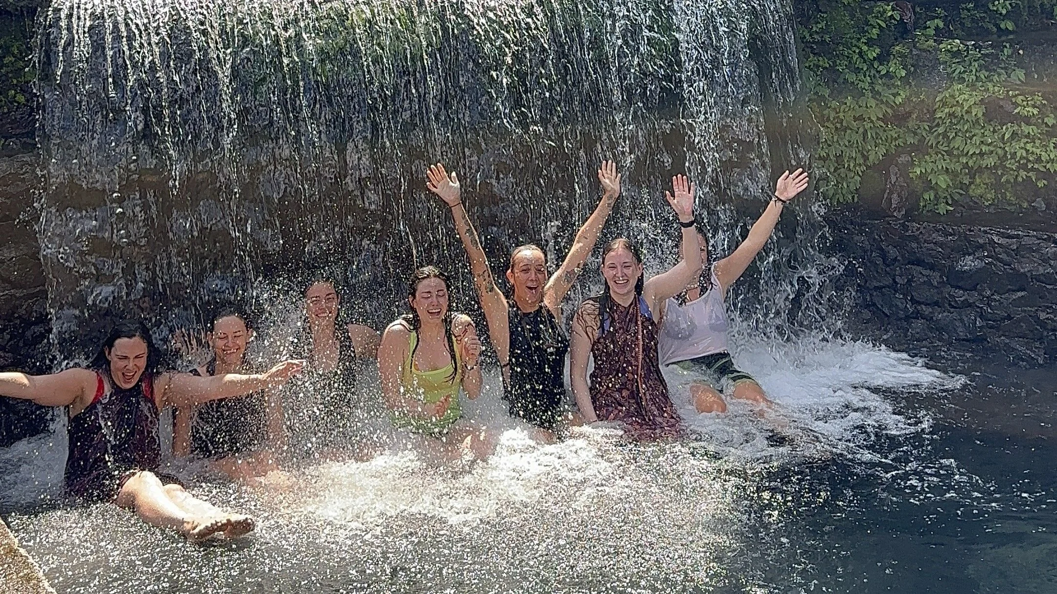 Travelers swimming beneath a hidden waterfall during a small group Lombok waterfall tour in Indonesia.