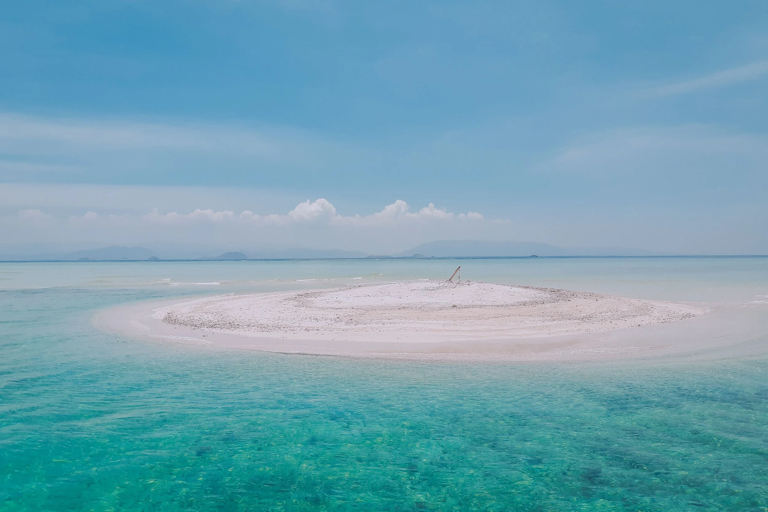Small sand island surrounded by clear turquoise water near Pink Beach