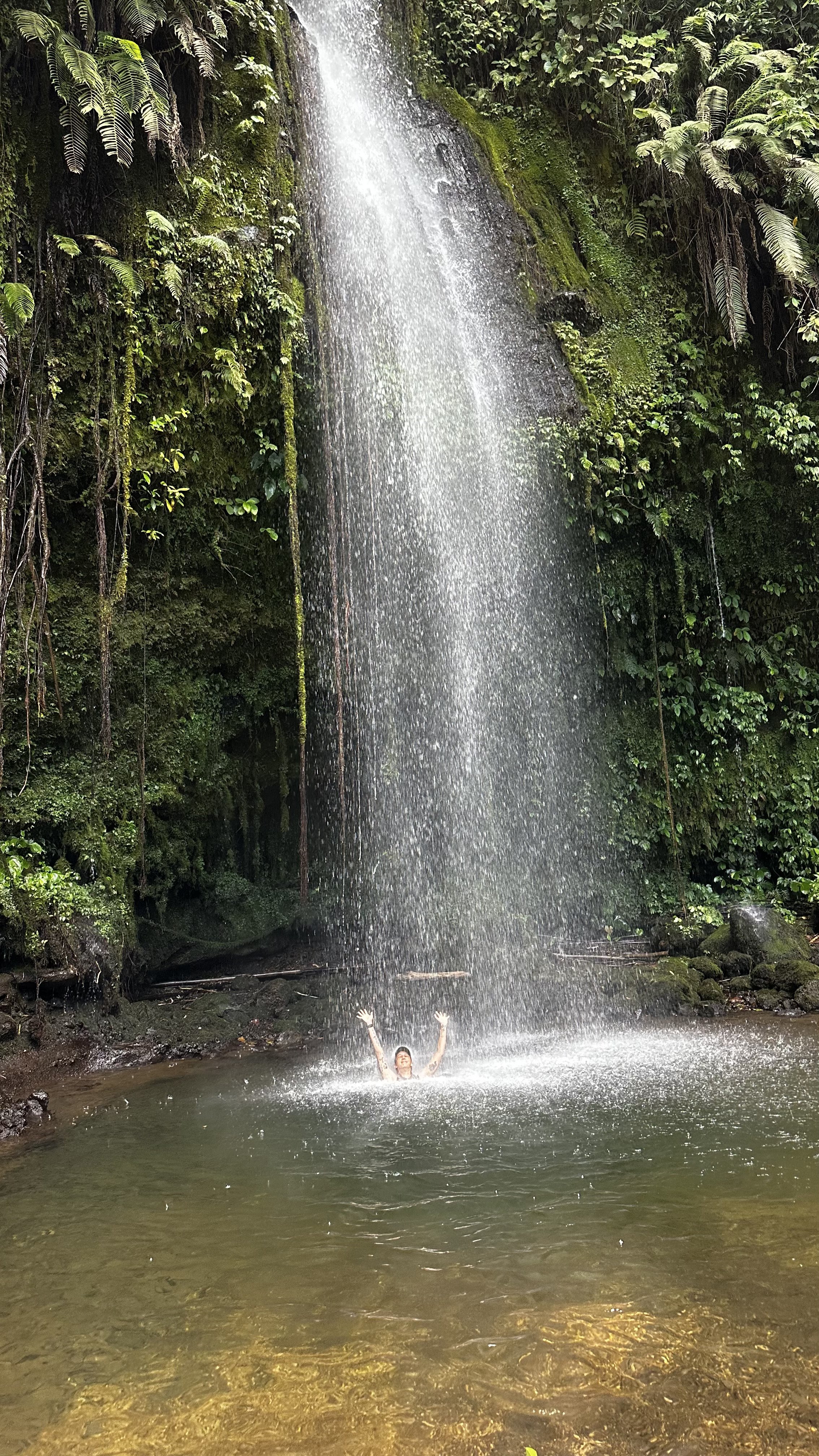 Traveller standing beneath a jungle waterfall during the Benang Stokel and Benang Kelambu tour in Lombok