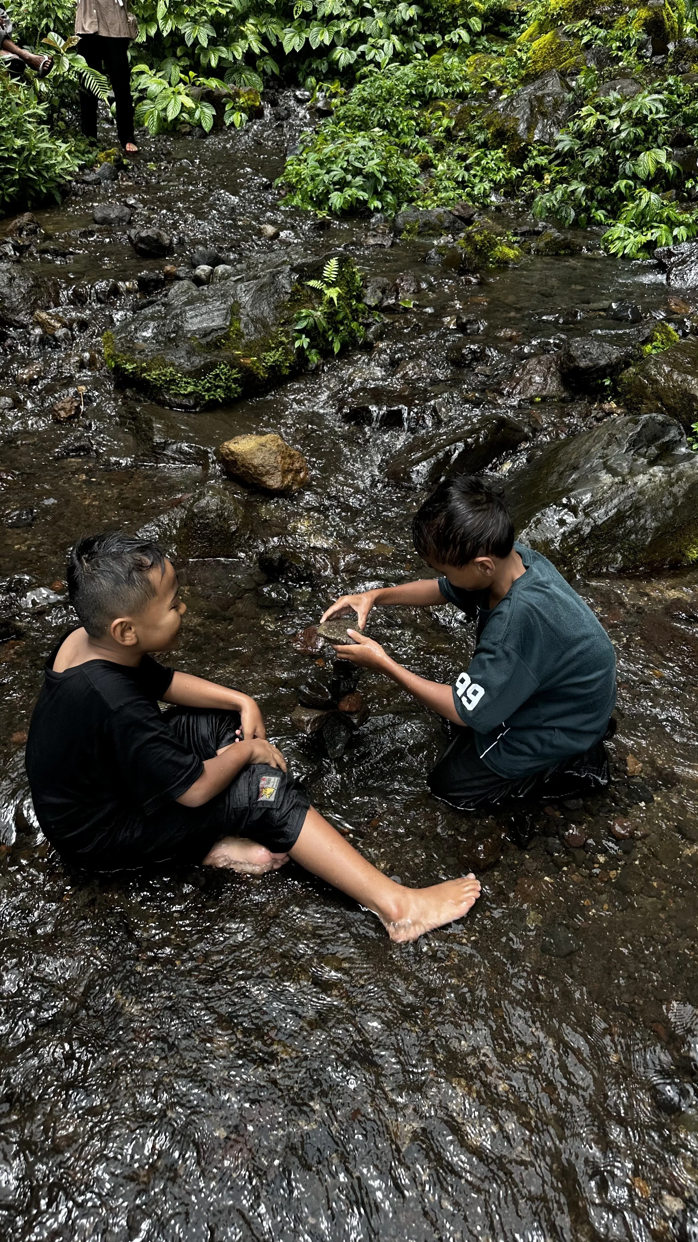 Local children playing in a shallow stream near Benang Stokel Waterfall in Lombok