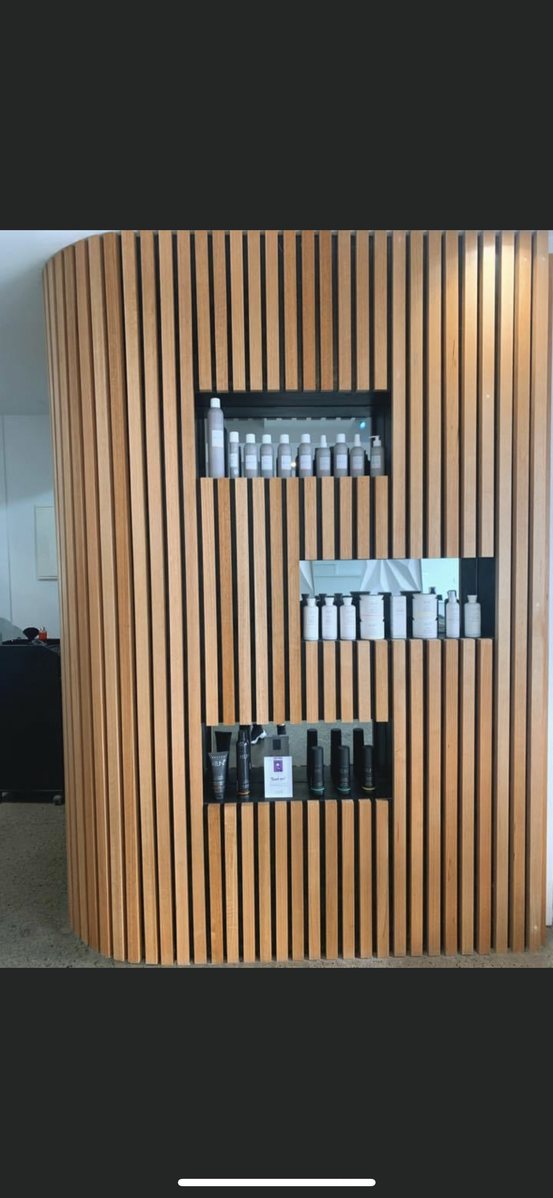 Wooden slatted display on a wall with various skincare or cosmetic bottles and containers.