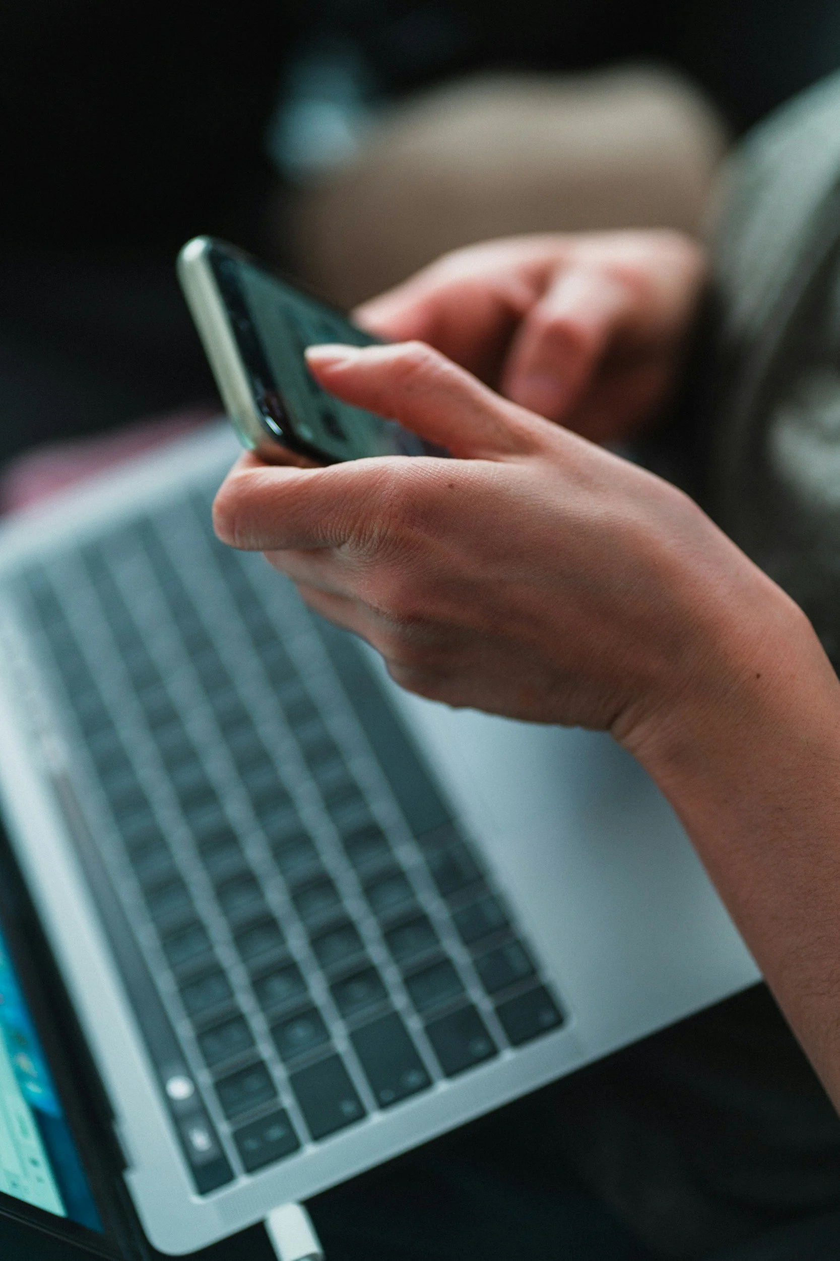 Close-up of a person's hand holding a smartphone, with a laptop keyboard visible in the background.