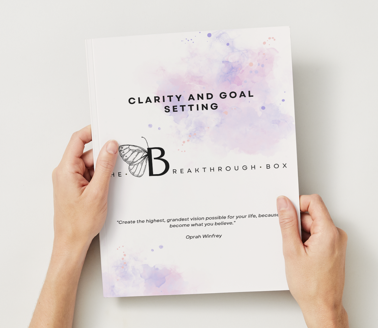 Hand holding a white booklet titled "Clarity and Goal Setting" with a butterfly illustration and a quote by Oprah Winfrey on a light background.