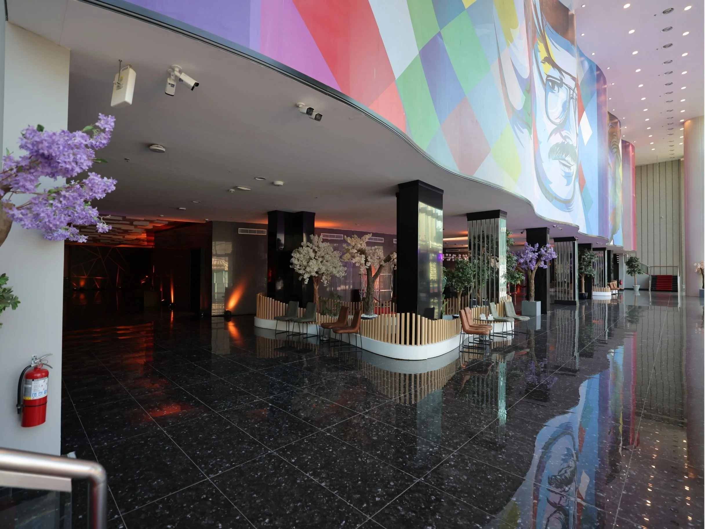 Interior of a modern lobby with black marble floors, purple-flowered trees, and a large colorful mural on the wall.bakr al sheddi, bouvard city