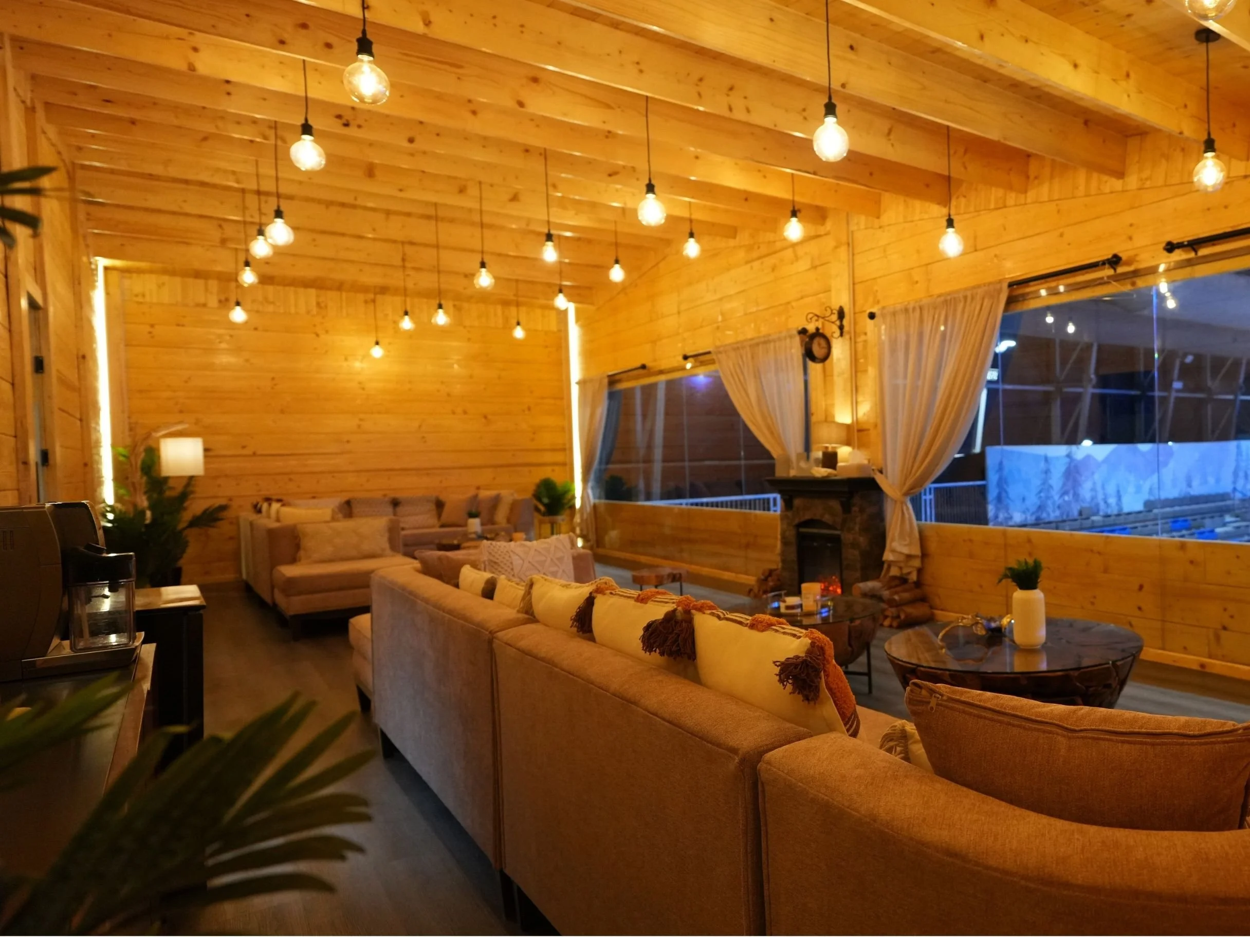 Interior of a cozy, wooden living room with warm lighting, beige sofas, a round coffee table, and curtains by large windows. cool arena iceskating rink.
