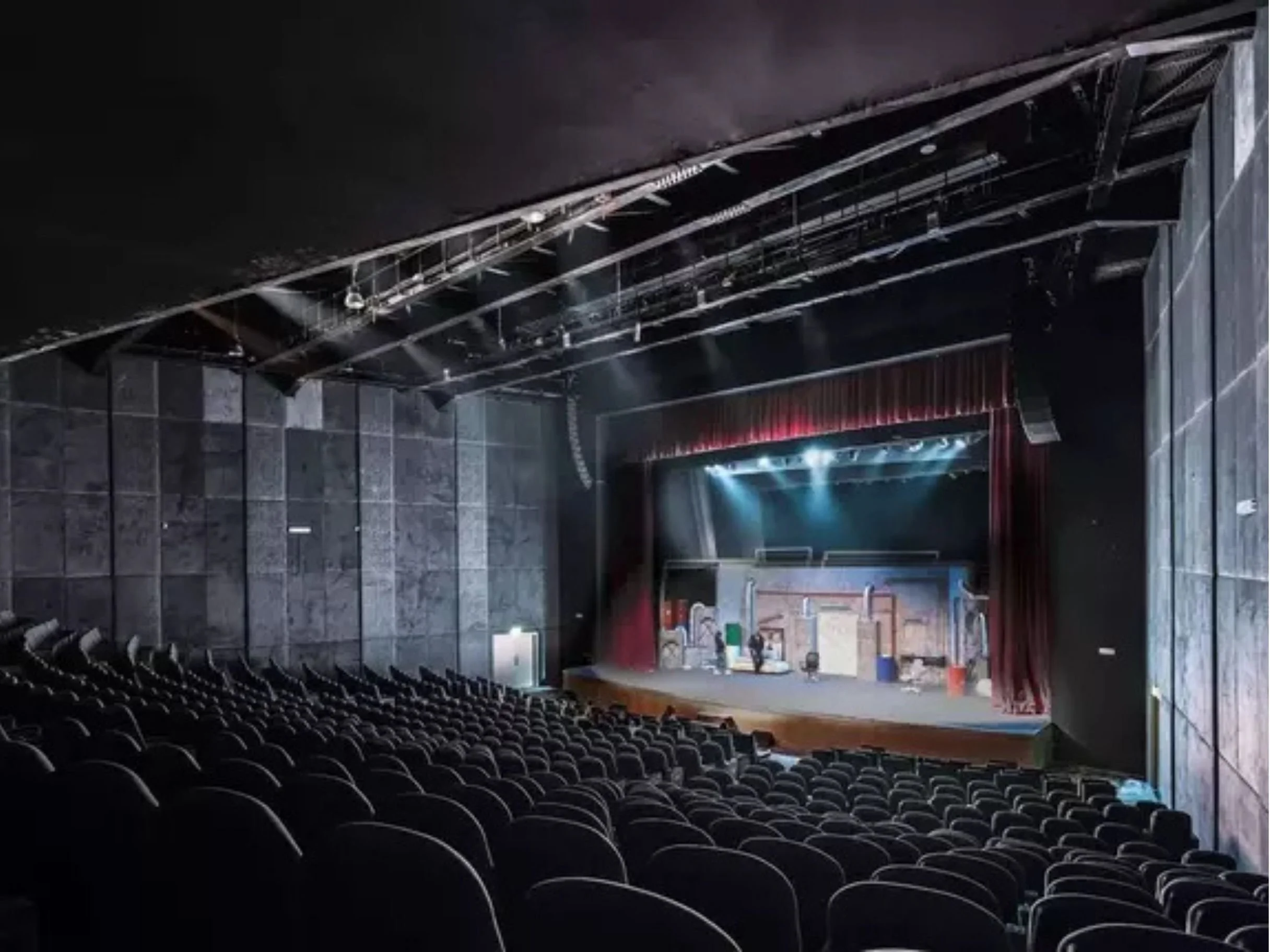 Empty theater auditorium with rows of black seats and a stage at the front, illuminated with stage lights, black walls, and red curtains.bakr al sheddi, bouvard city, mohamad al ali