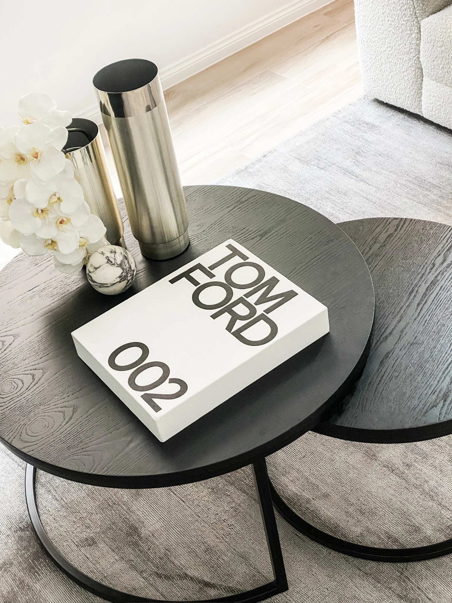 Modern coffee table with decorative vase, white flowers, a marble sphere, and a book titled 'Tom Ford 002'.