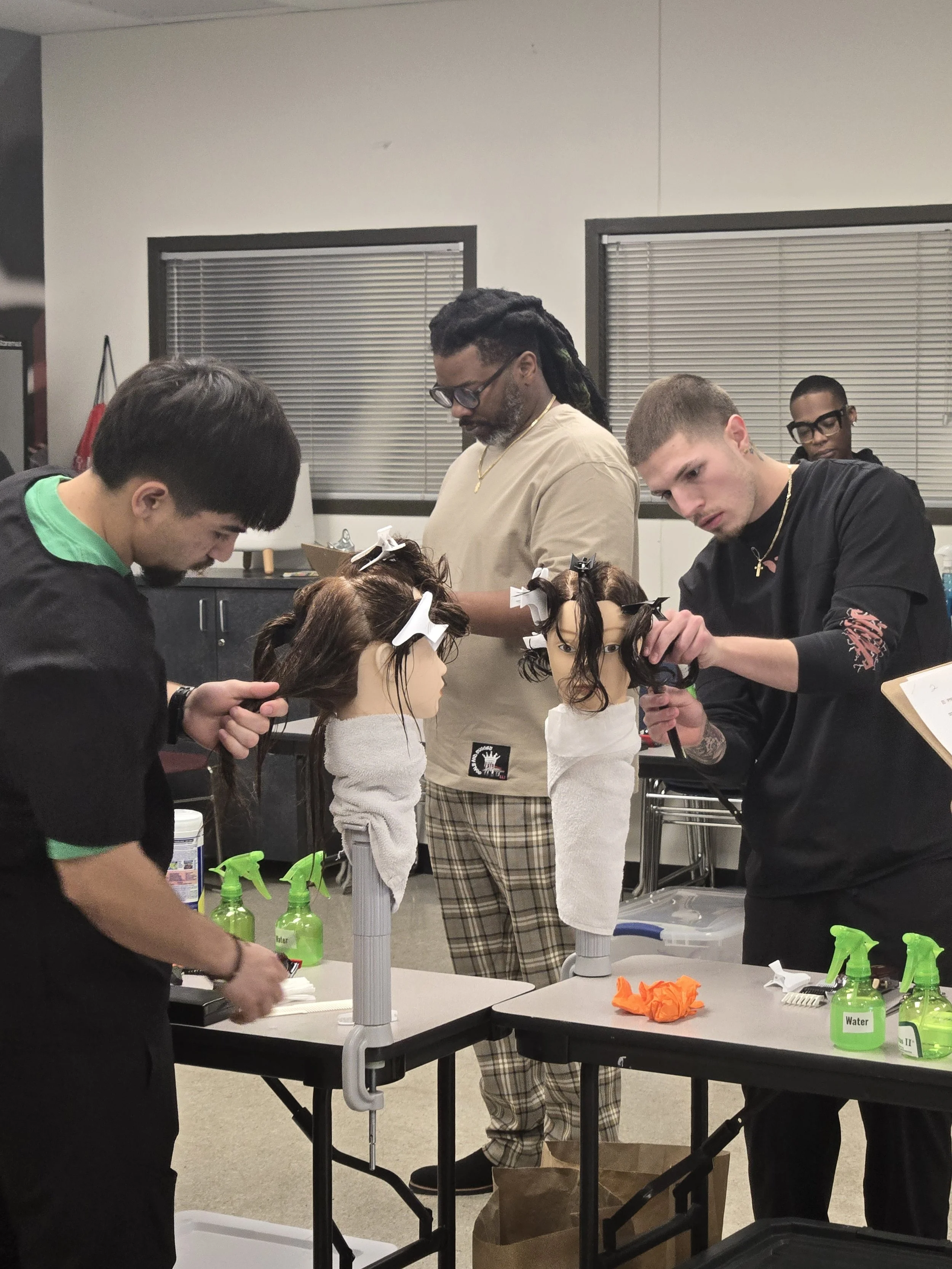 G-Cuts Educating four people working on mannequins with hair station supplies on tables.