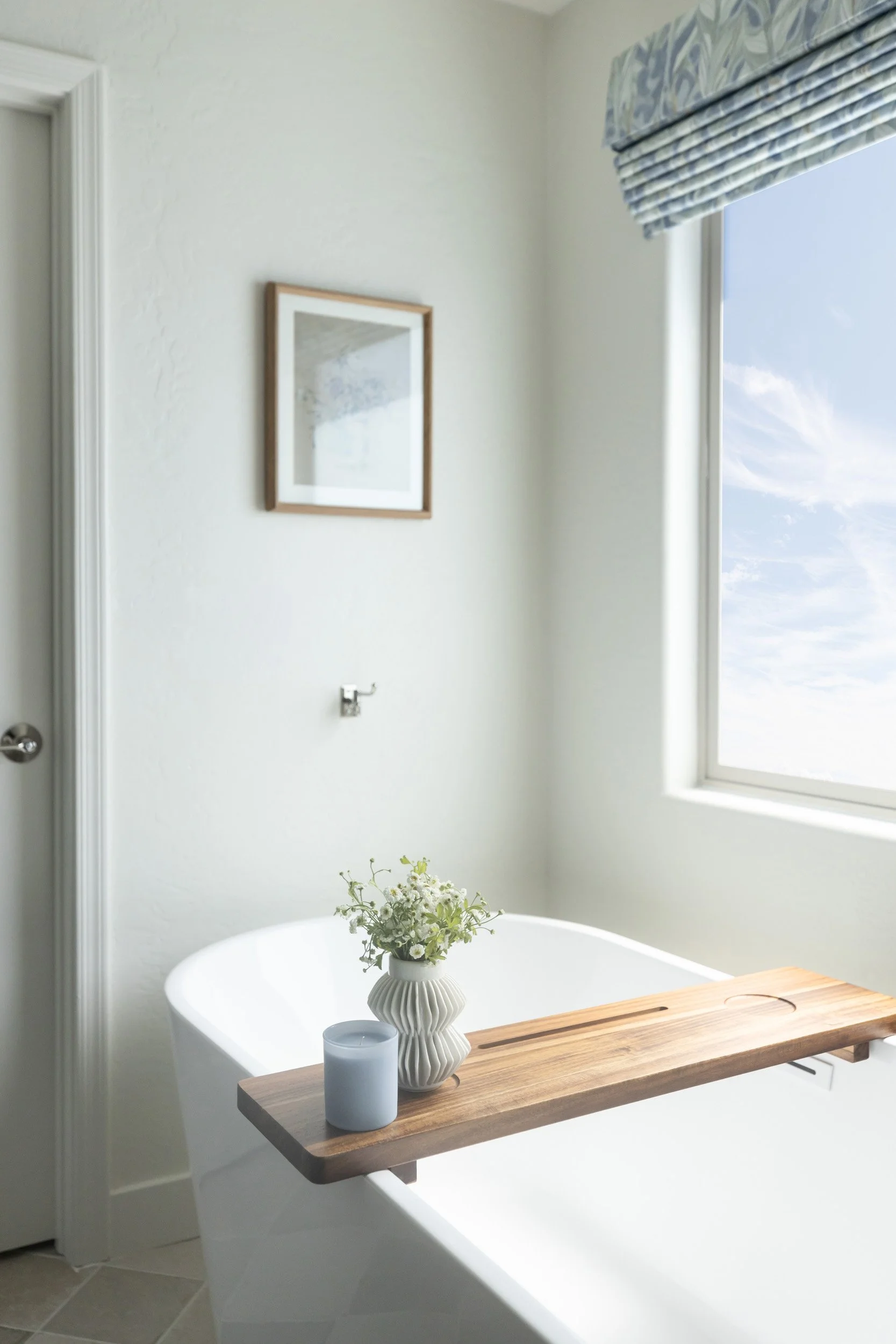 Freestanding tub with wood bath tray beneath a window in an Arizona primary bathroom