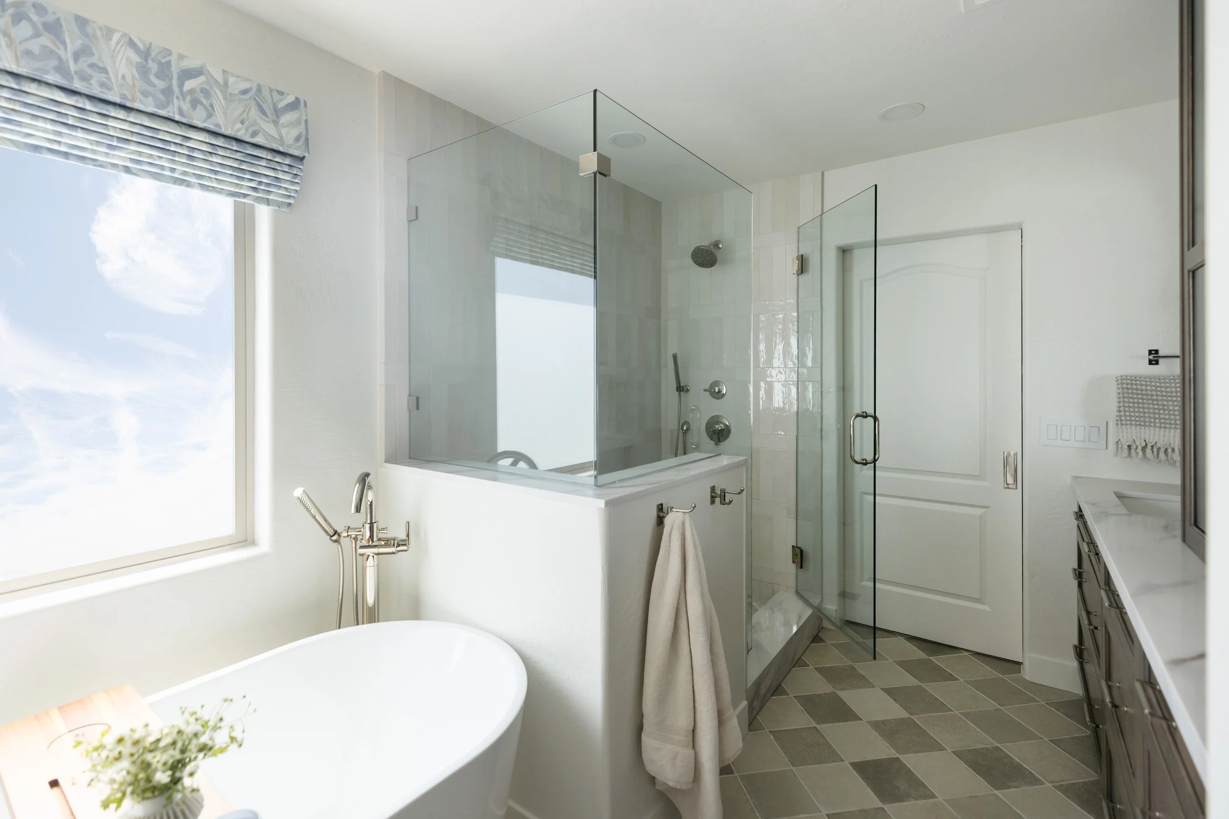 Primary bathroom in a Desert Ridge, Phoenix home with a freestanding tub, glass shower, patterned Roman shade and checkerboard tile floor
