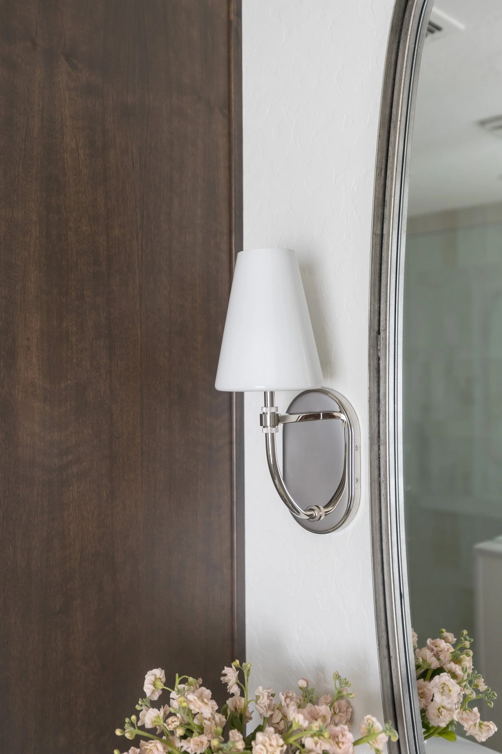 Wall sconce with white shade beside a rounded mirror in an Arizona primary bathroom