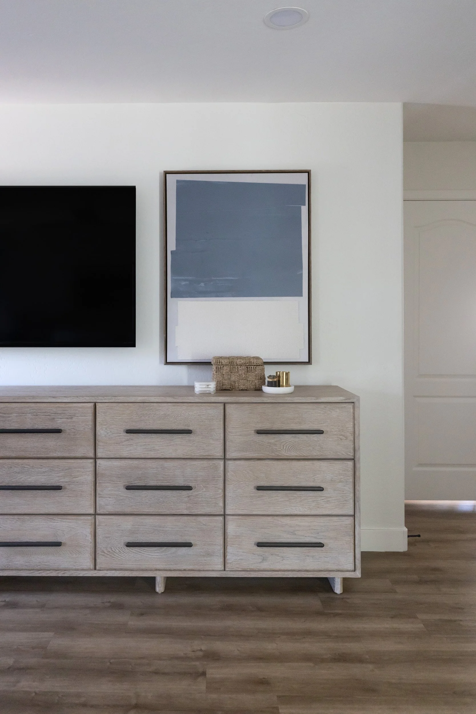 Whitewashed wood dresser with framed art and mounted TV in a Desert Ridge bedroom