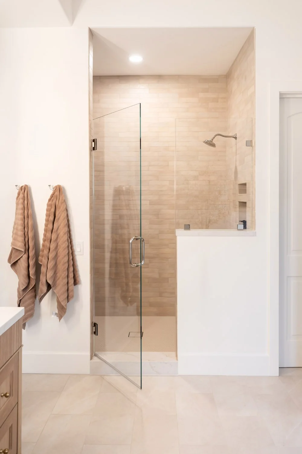 Interior design project of modern Mediterranean bathroom entry with hooks and textured towels leading to a light shower.