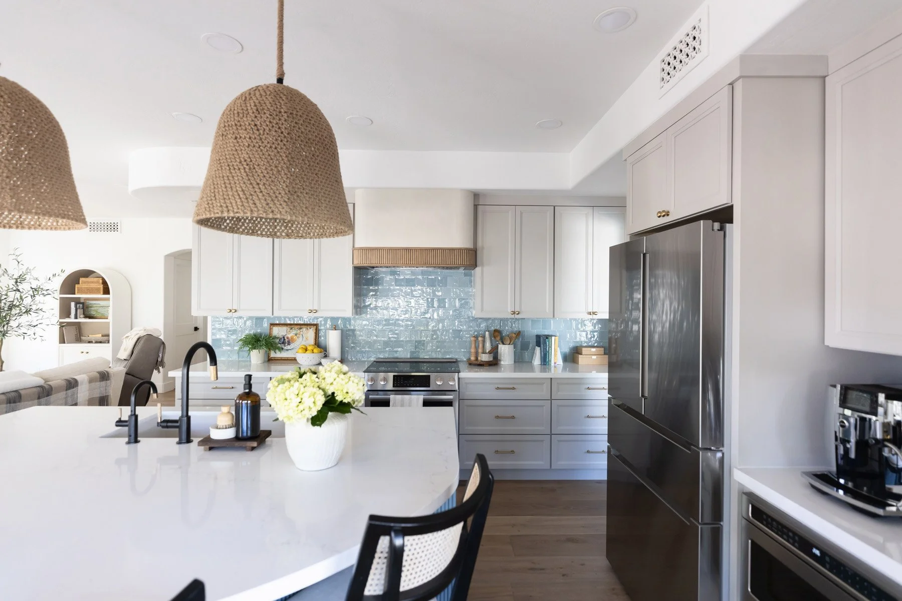 Kitchen with woven pendant light, white quartz island, black faucet, yellow floral arrangement, blue fluted island base, stainless steel fridge, and blue zellige tile backsplash