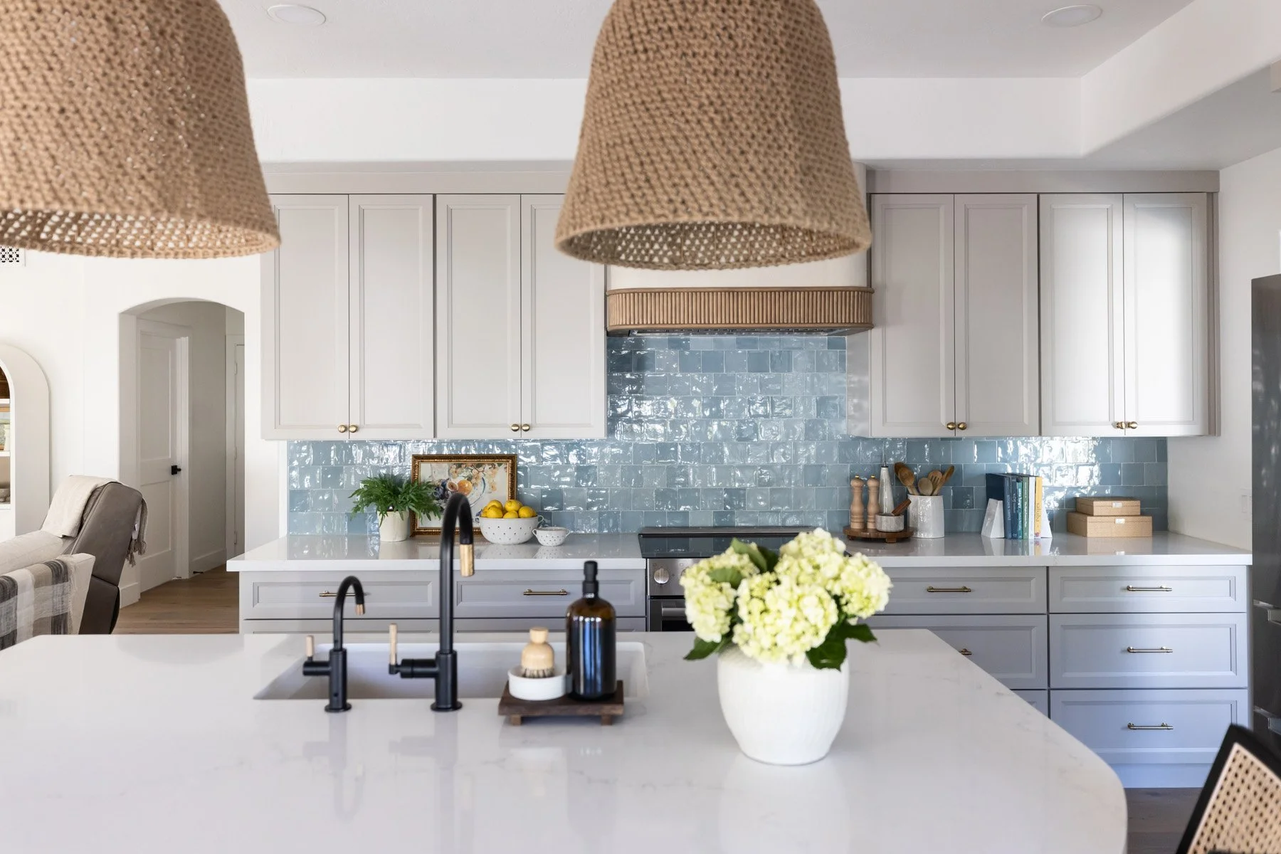 Kitchen overhead view with white quartz island, black faucet, yellow floral arrangement, blue zellige tile backsplash, and woven pendant lights