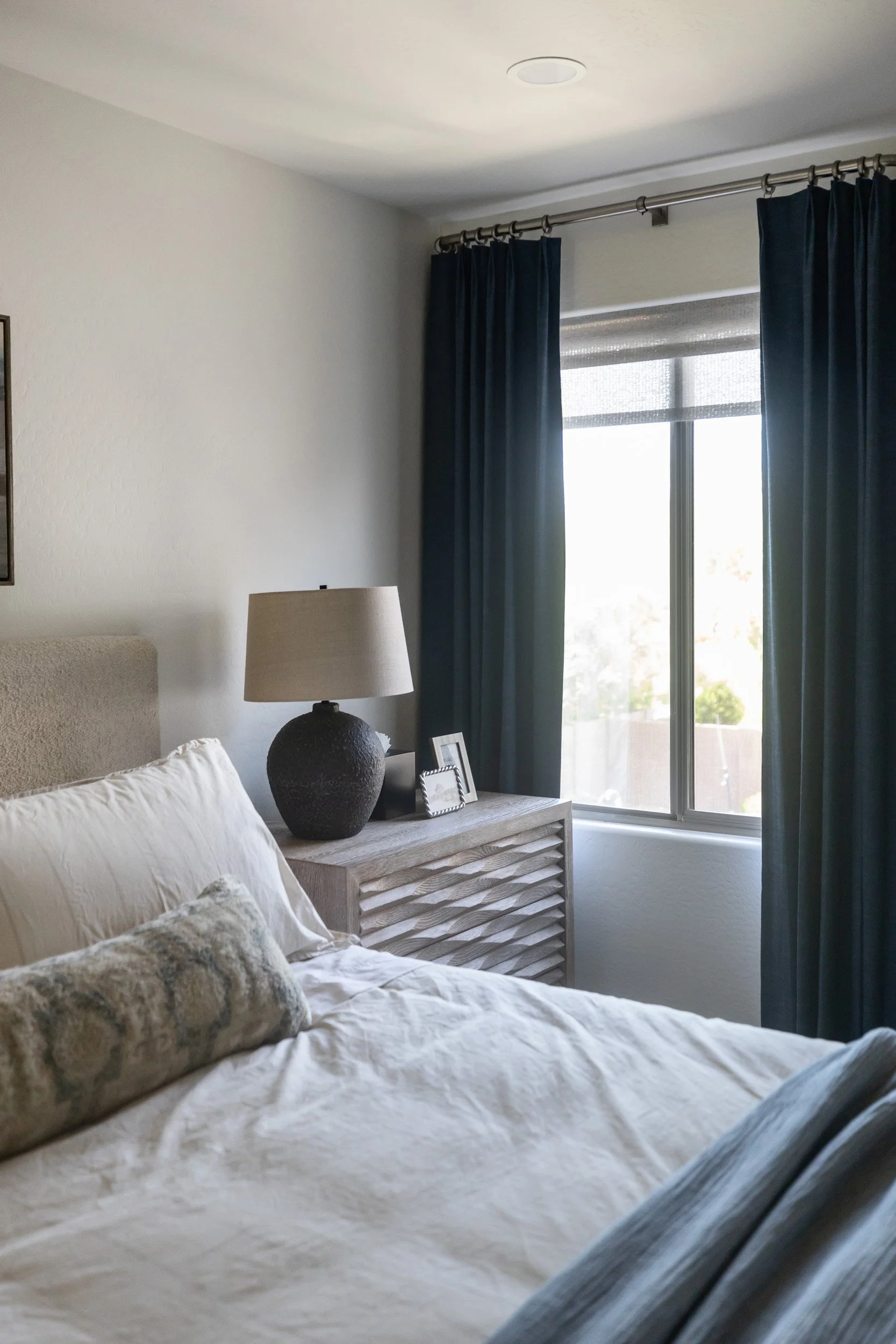 Primary bedroom window with navy drapes beside the bed and nightstand, Desert Ridge