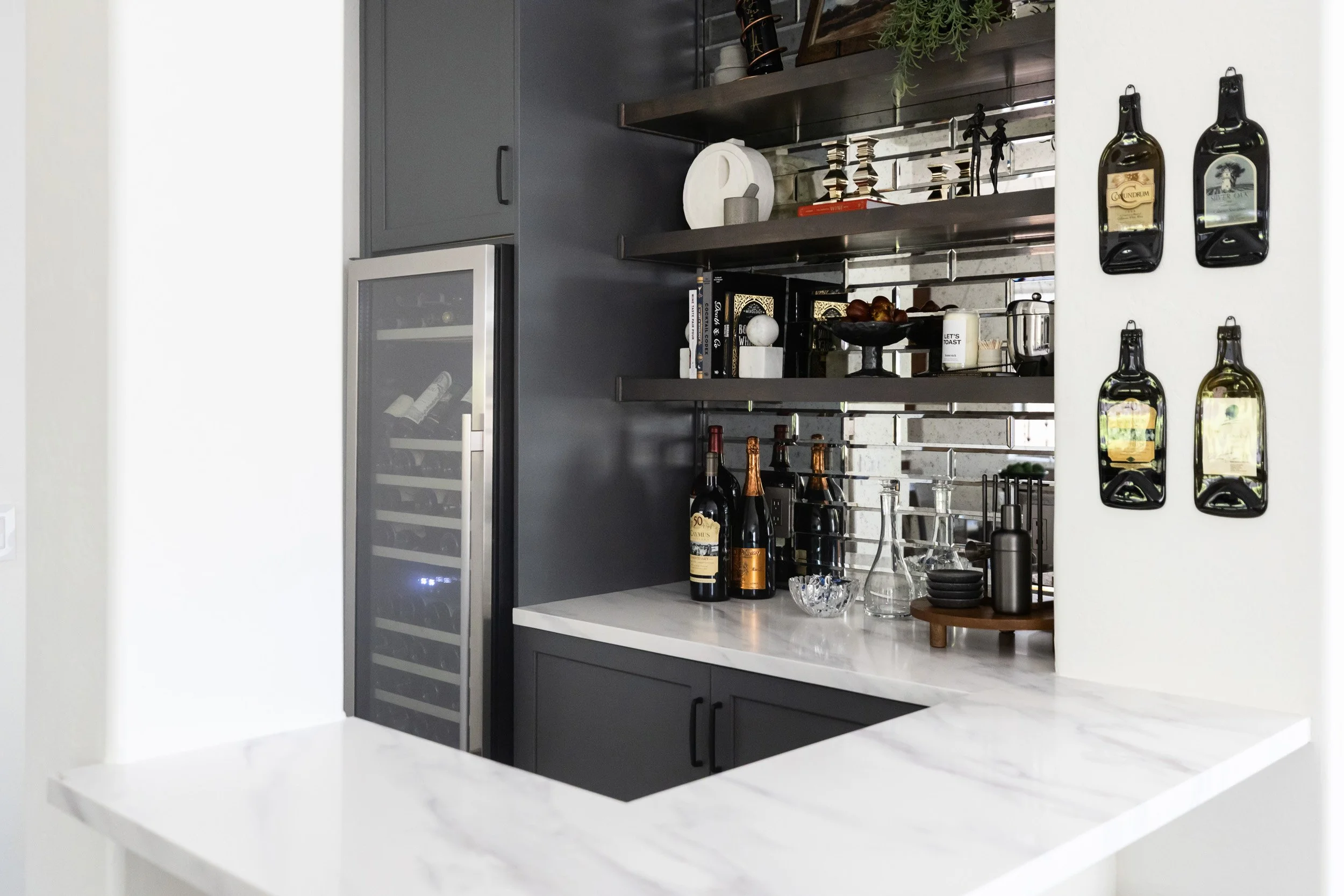 Home wine bar with black cabinets, wine fridge, open shelving and marble countertop in Desert Ridge