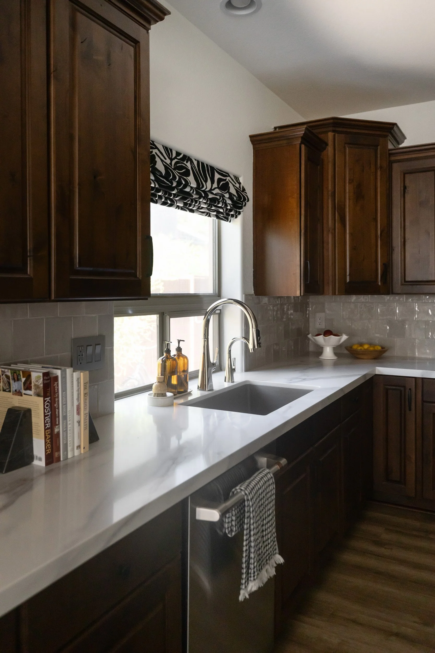 Kitchen sink under a window with patterned Roman shade and white countertops, Phoenix