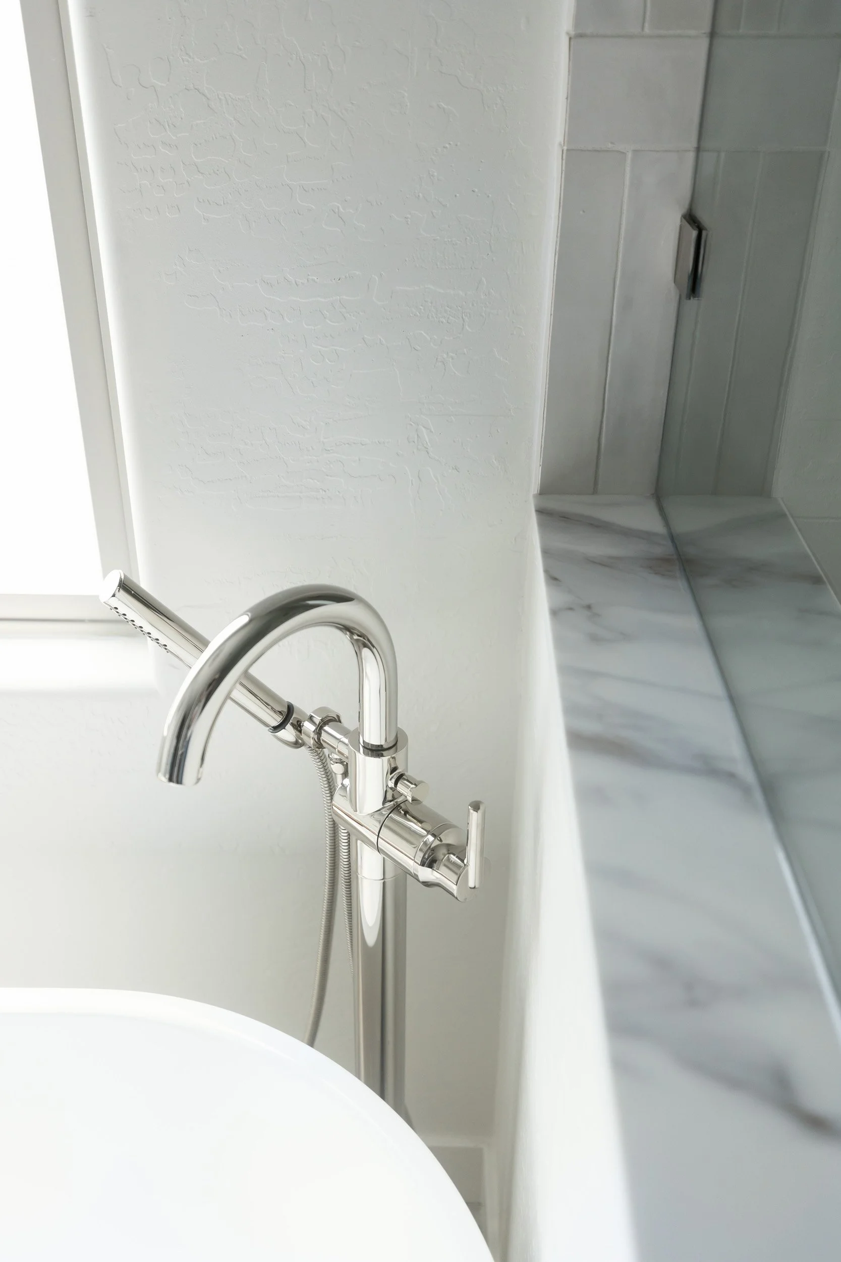 Floor-mounted tub filler beside a freestanding tub and marble shower wall, Phoenix