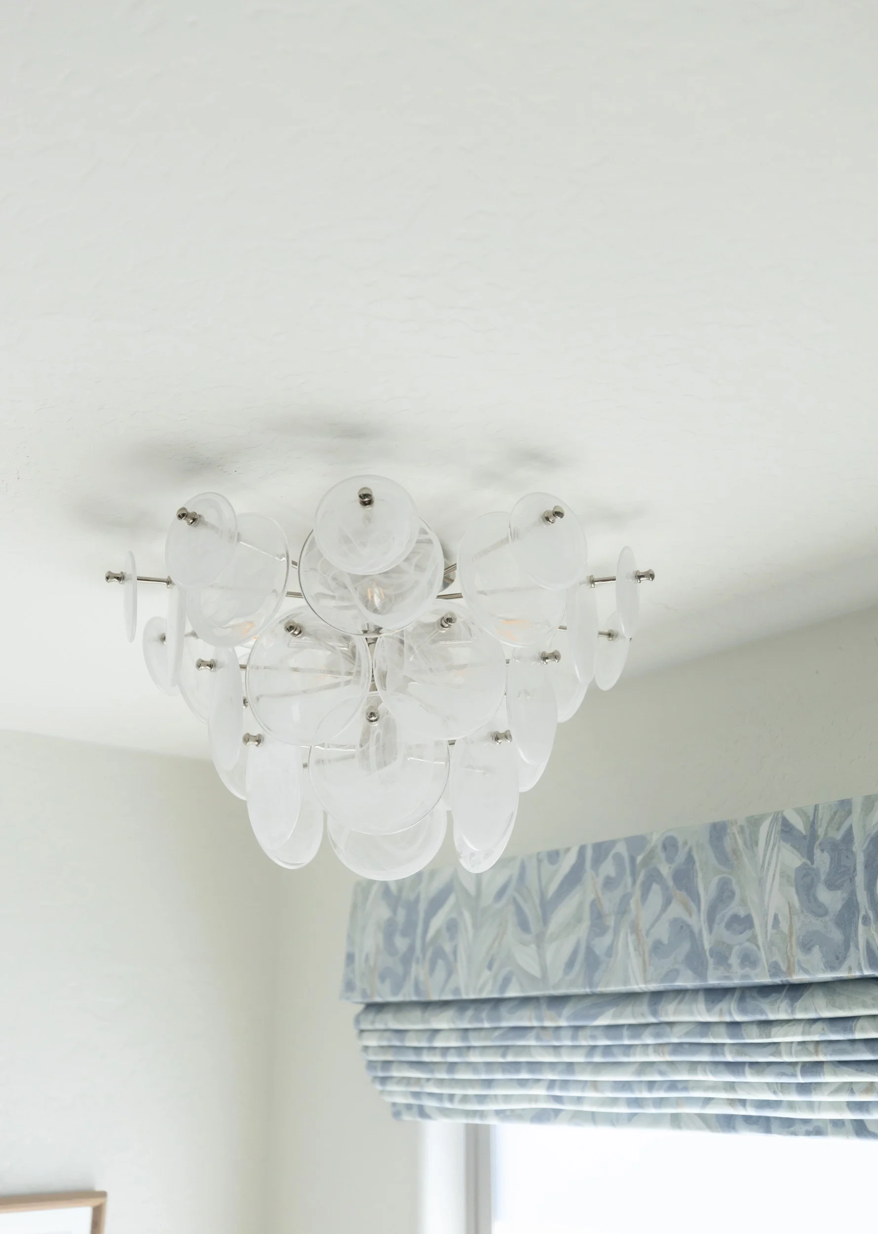 Glass chandelier above a window with blue patterned Roman shade in a Desert Ridge bathroom