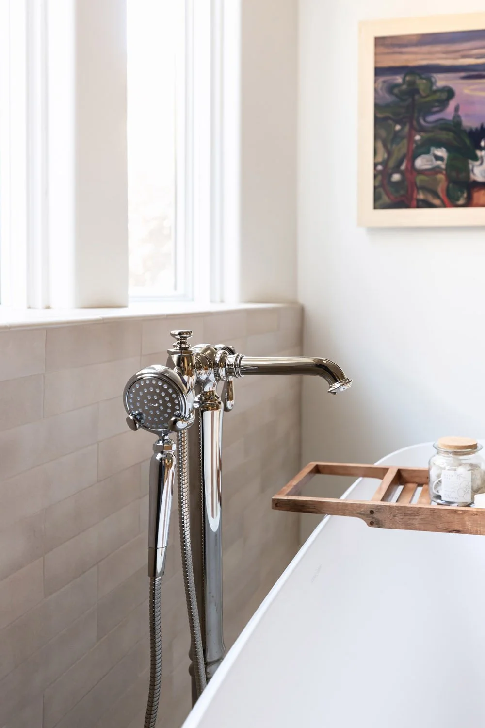 Polished nickel freestanding tub faucet with handheld shower wand and wood caddy tray against zellige-style tile