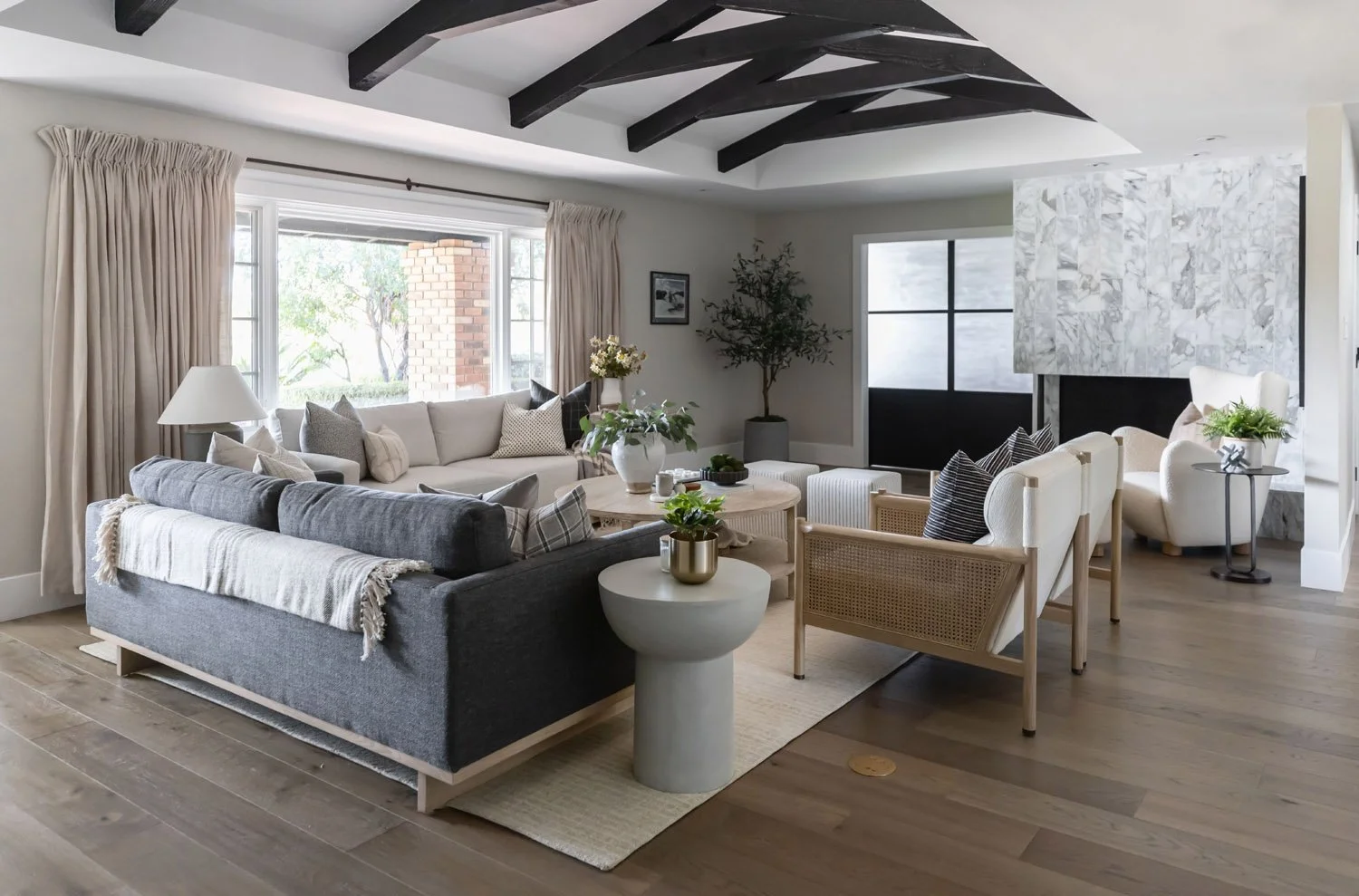 Living room with dark grey sectional, linen sofa and exposed wooden ceiling beams