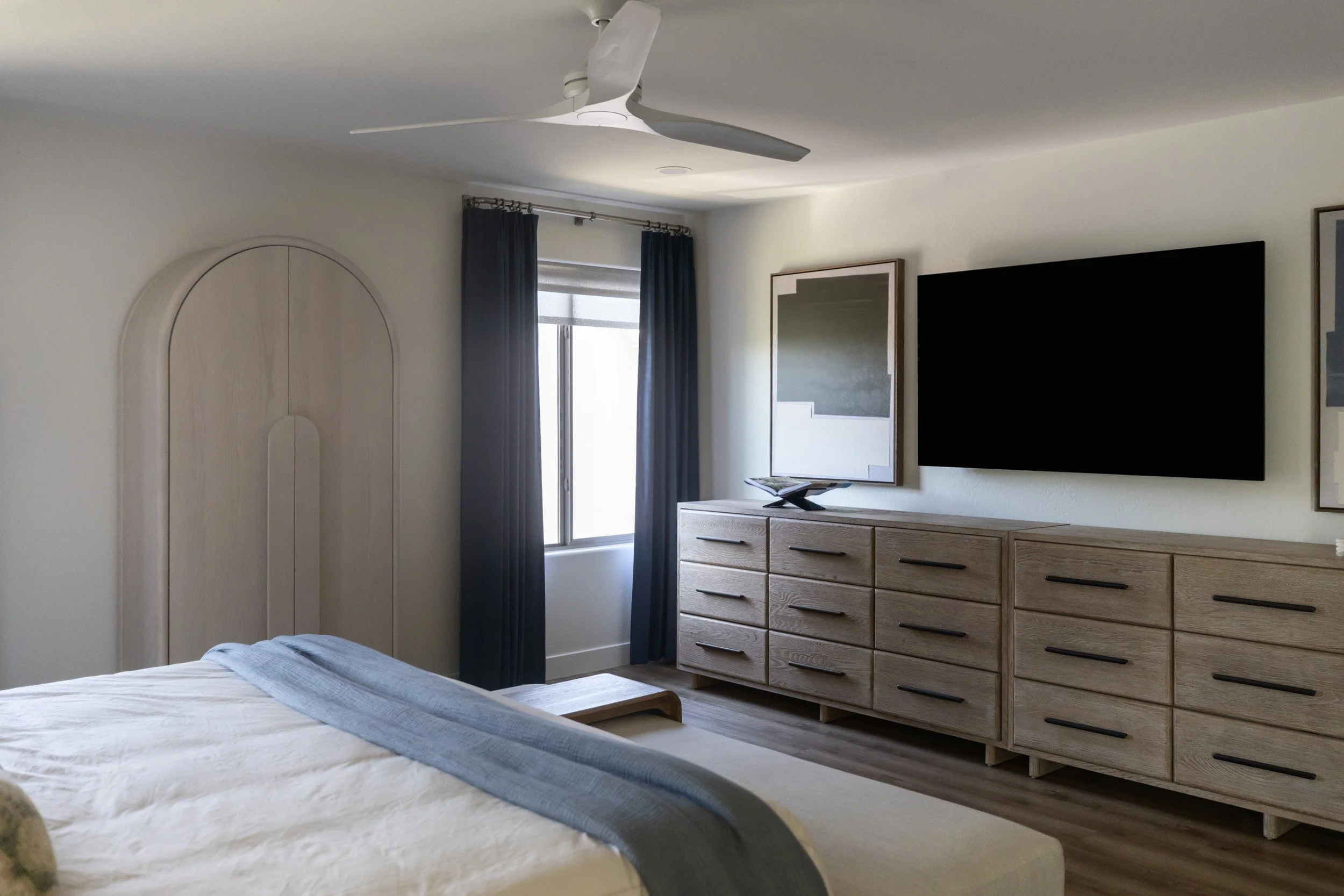 Primary bedroom dresser wall with mounted TV, arched mirror and navy curtains, Phoenix