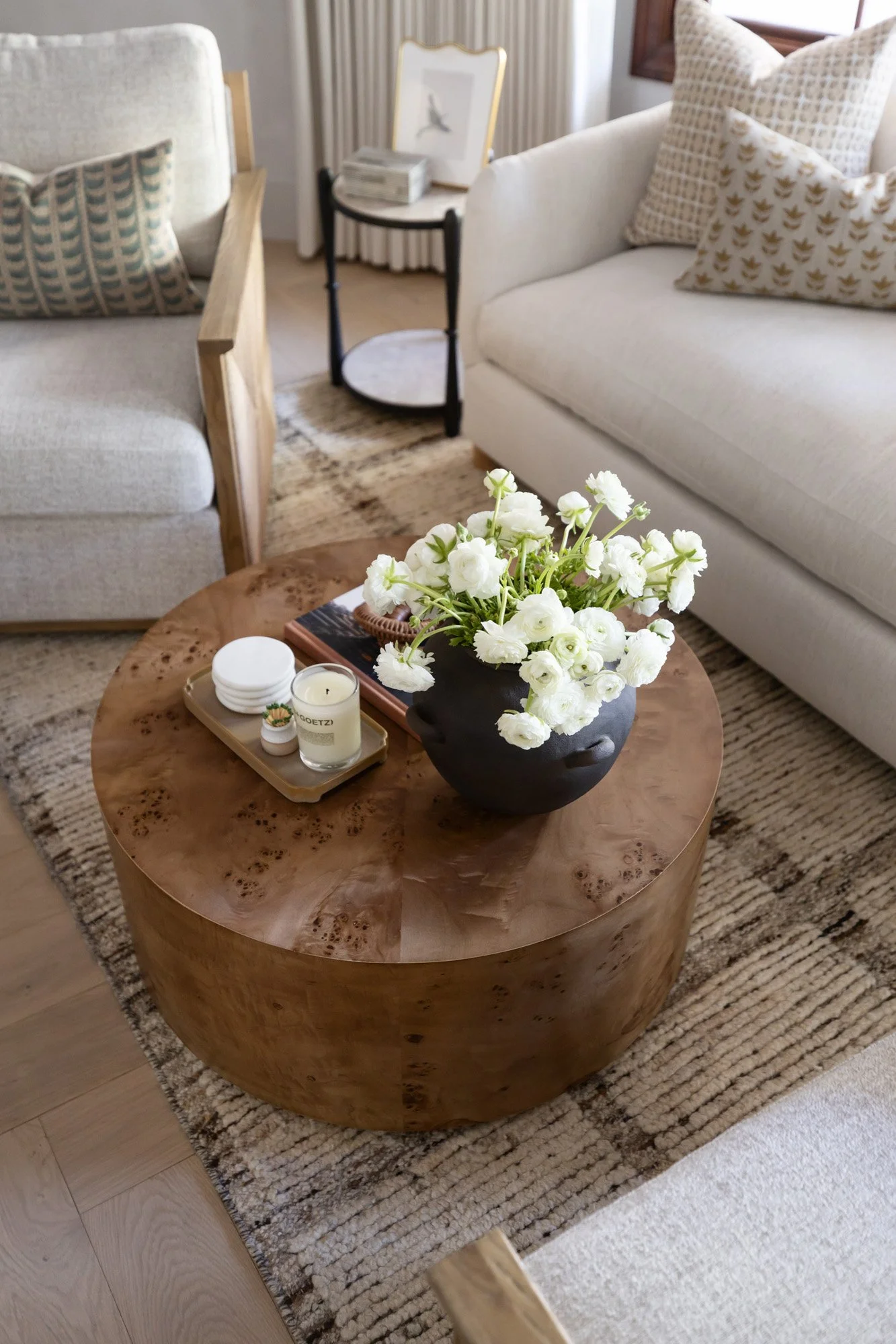 Sitting room with white sofa, round wood slab coffee table, white floral arrangement, black ceramic bowl, and neutral rug