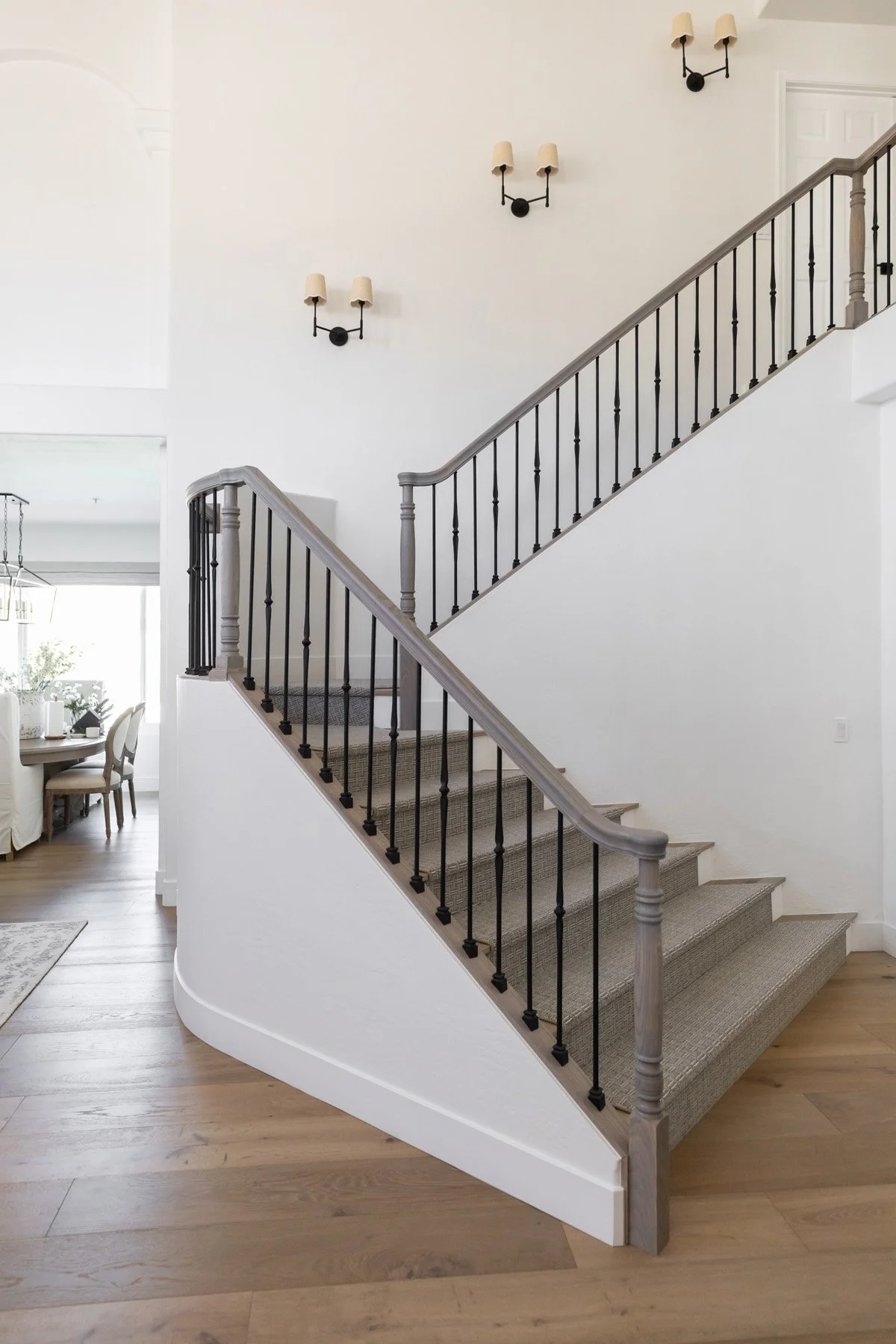 Bright staircase with white painted walls, grey painted timber treads, black iron balustrade, black double arm wall sconce, and light oak floor below