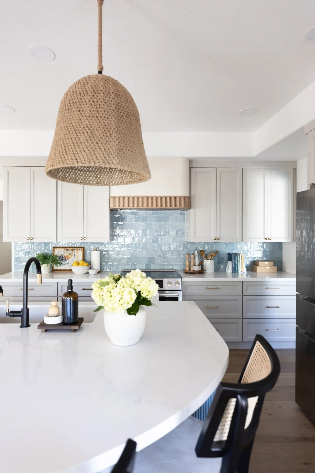 Scottsdale kitchen with curved blue fluted island, woven pendant light, white quartz countertop, black matte faucet, white hydrangea arrangement, white shaker cabinetry, and blue zellige tile backsplash