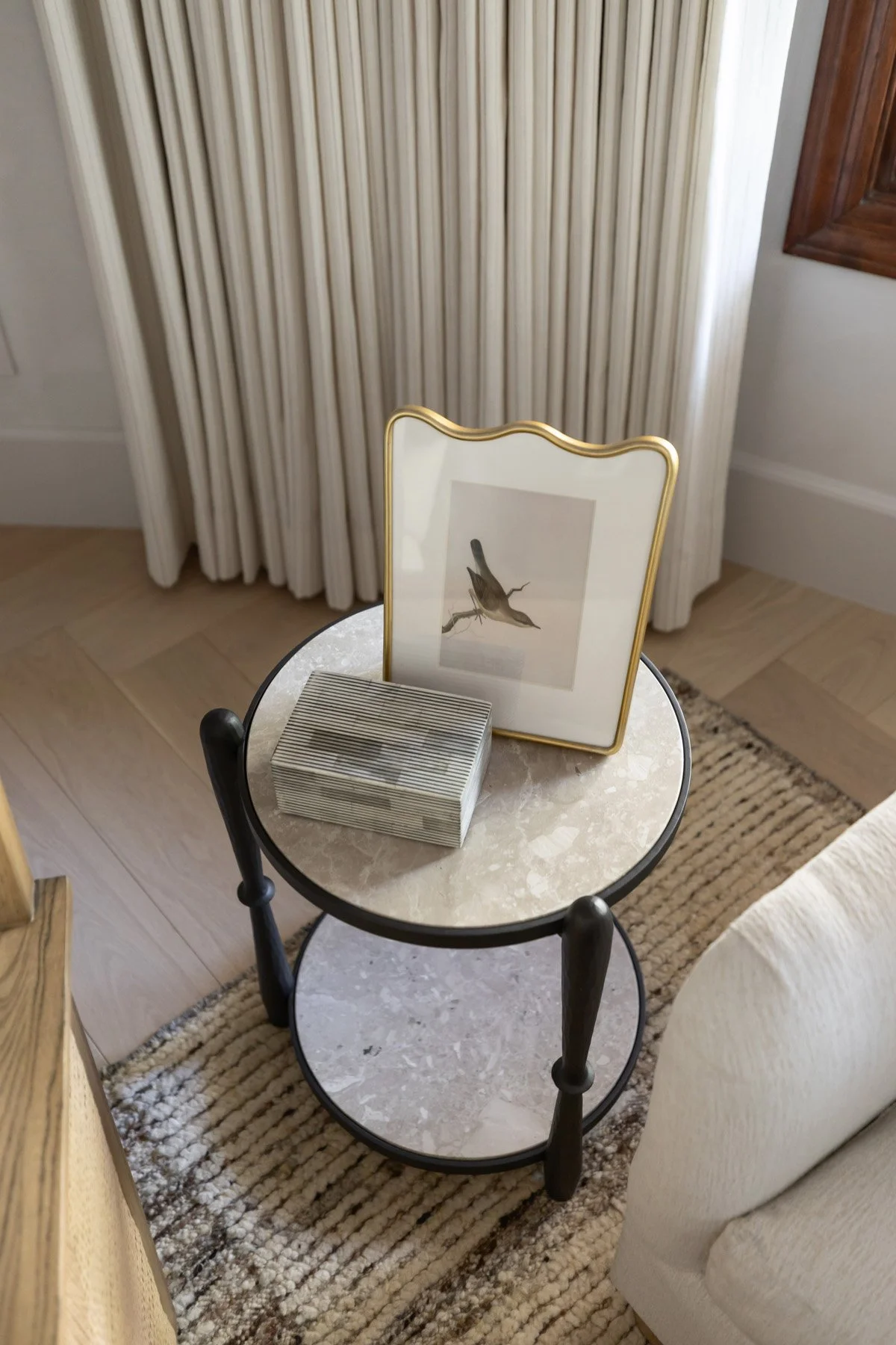 Round marble and black iron side table with framed bird artwork and framed print beside ivory armchair 
