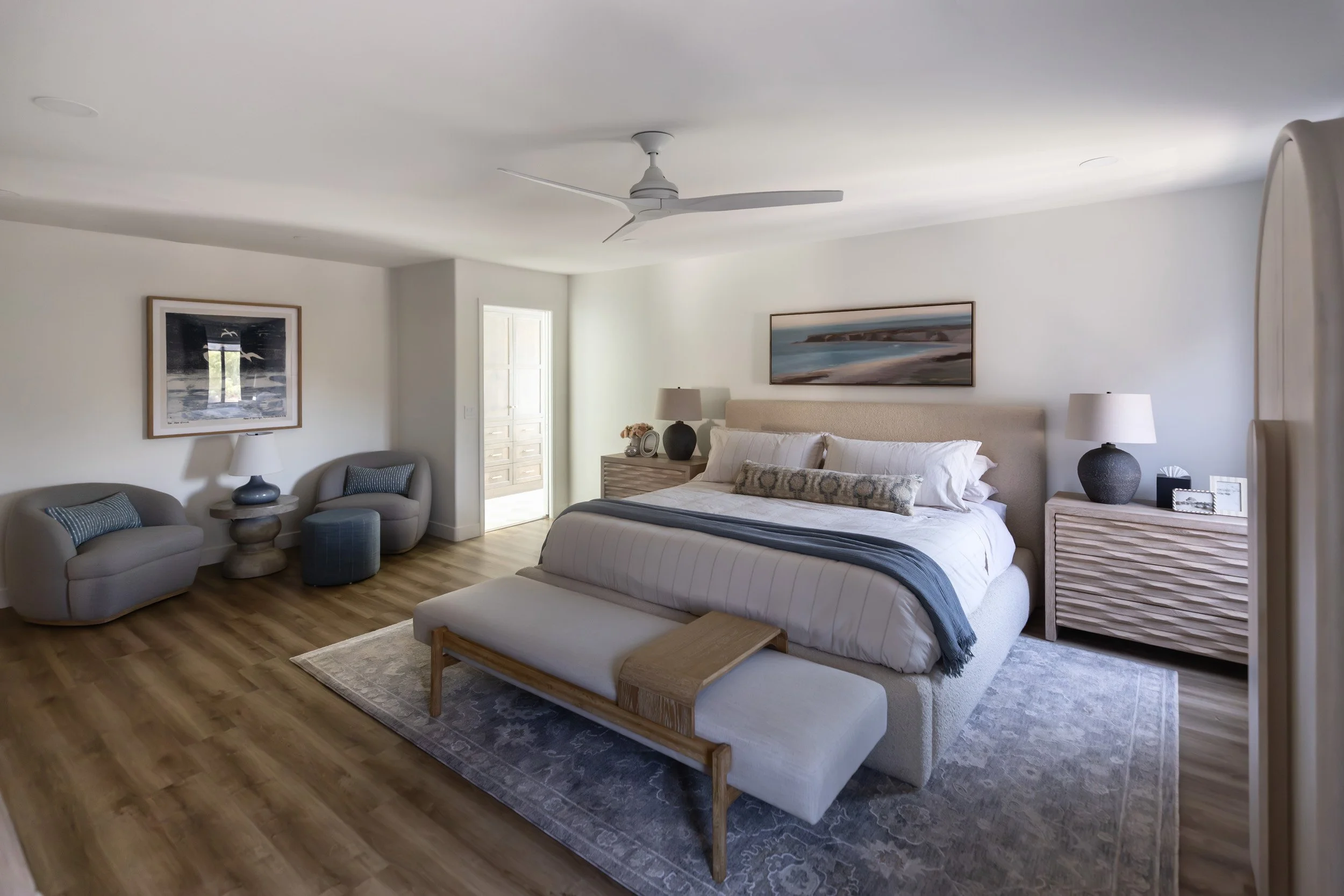 Primary bedroom in a Desert Ridge, Phoenix home with an upholstered bed, carved wood nightstands, blue rug and a swivel chair seating area