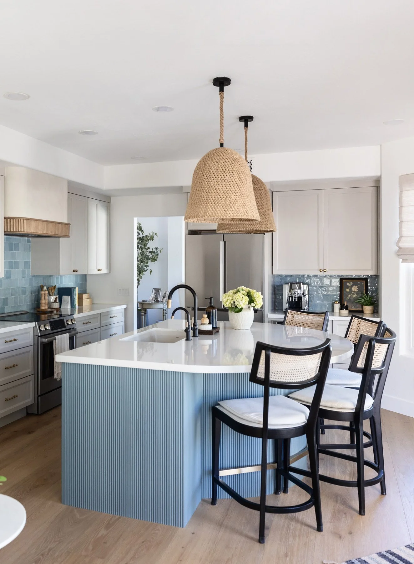 Scottsdale kitchen with curved blue fluted island, white quartz countertop, black cane bar stools, woven pendant lights, white shaker cabinetry, and blue zellige tile backsplash
