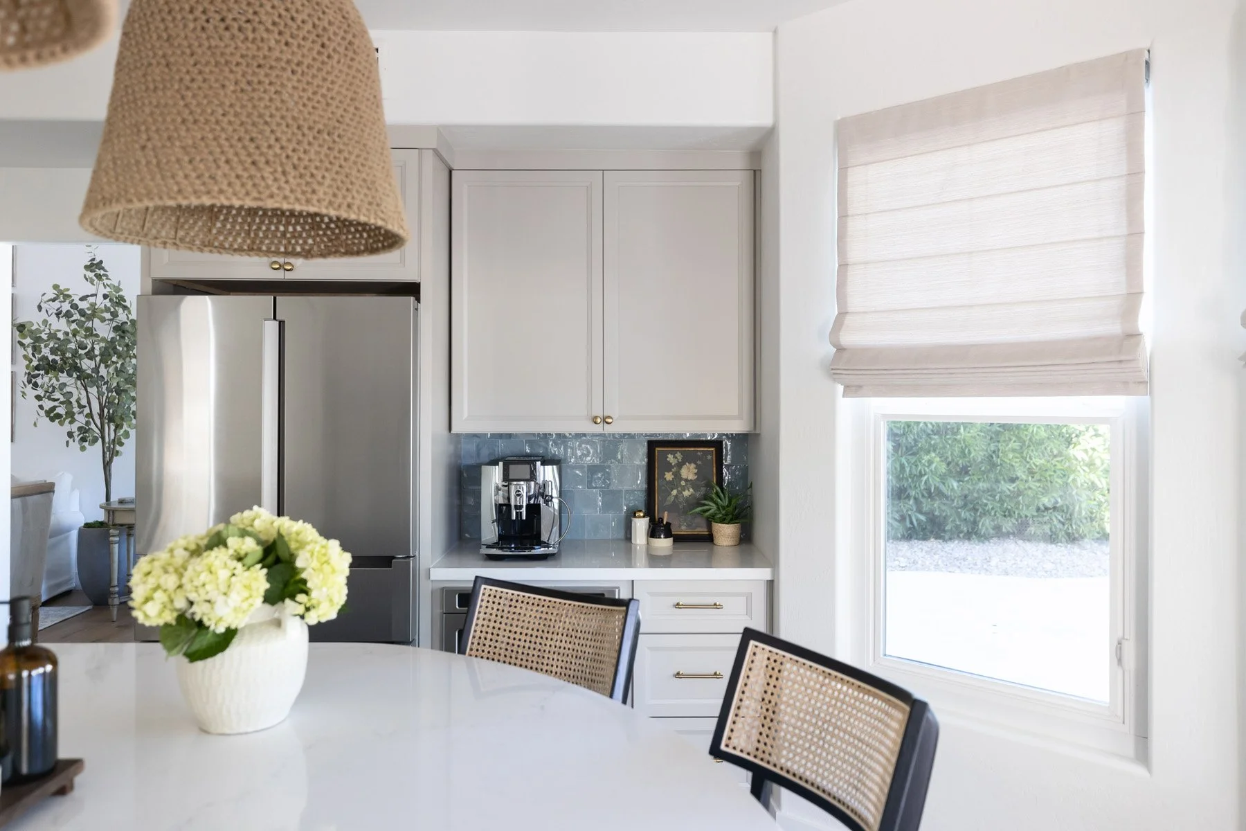 Kitchen dining area with round white table, cane dining chairs, white floral arrangement, woven pen