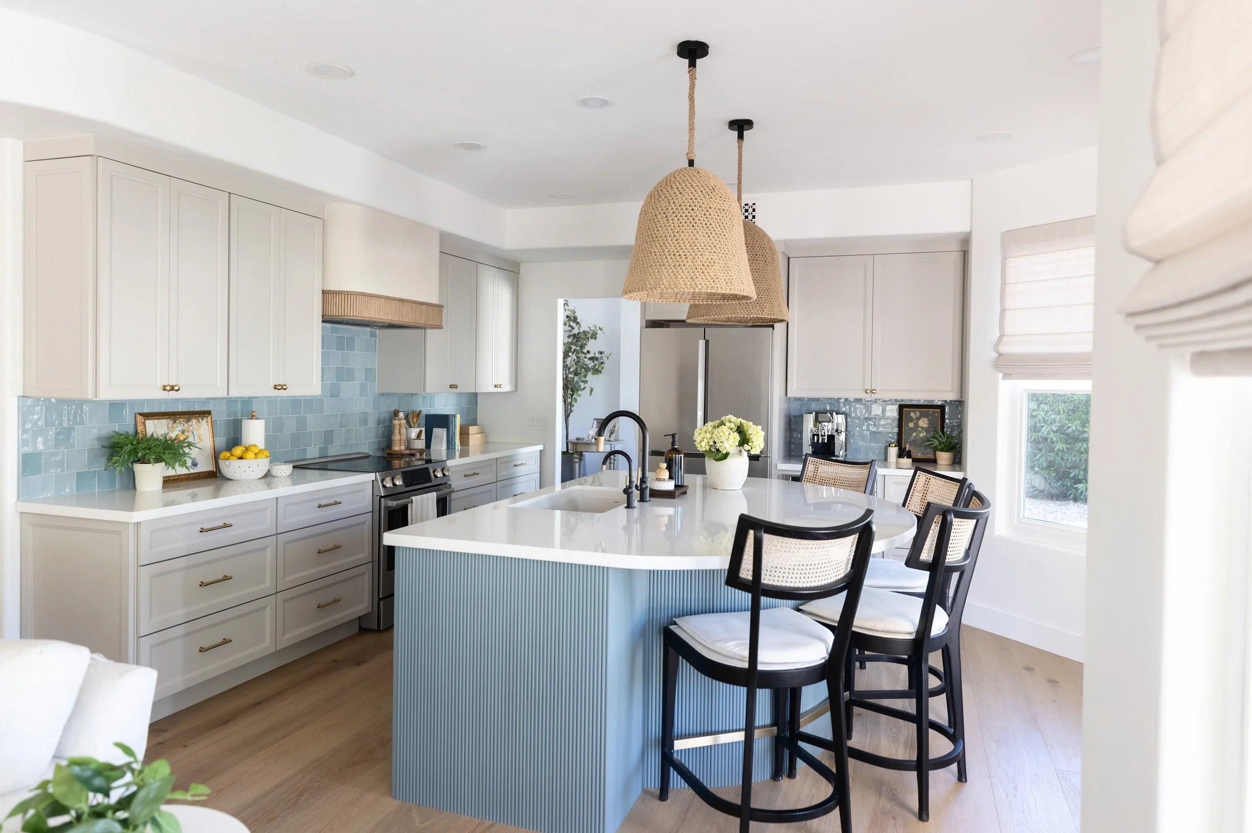 Kitchen with blue fluted island, white quartz countertop, black cane bar stools, woven pendant light, white shaker cabinetry, blue zellige tile backsplash, and light oak floors