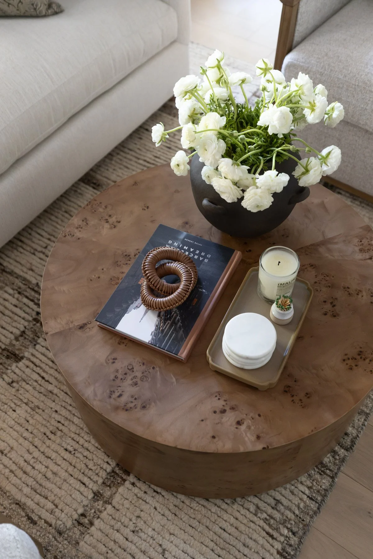 Overhead detail of round wood slab coffee table with white floral arrangement, black ceramic vase, decorative book, and candle