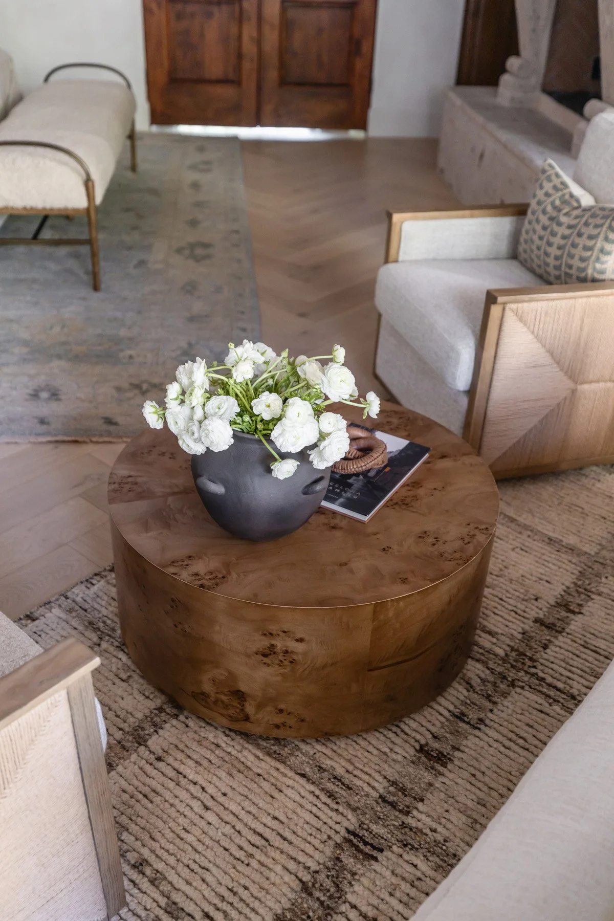 Overhead detail of round wood slab coffee table with white floral arrangement, black ceramic bowl, and decorative book