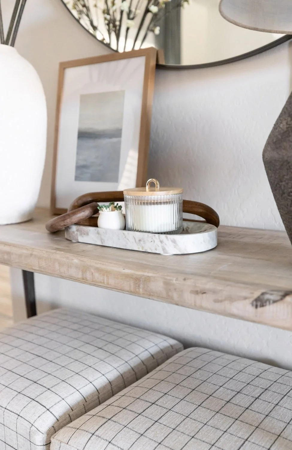 Entryway console detail in a Phoenix home with light oak surface, decorative tray, white ceramic candle, and framed prints