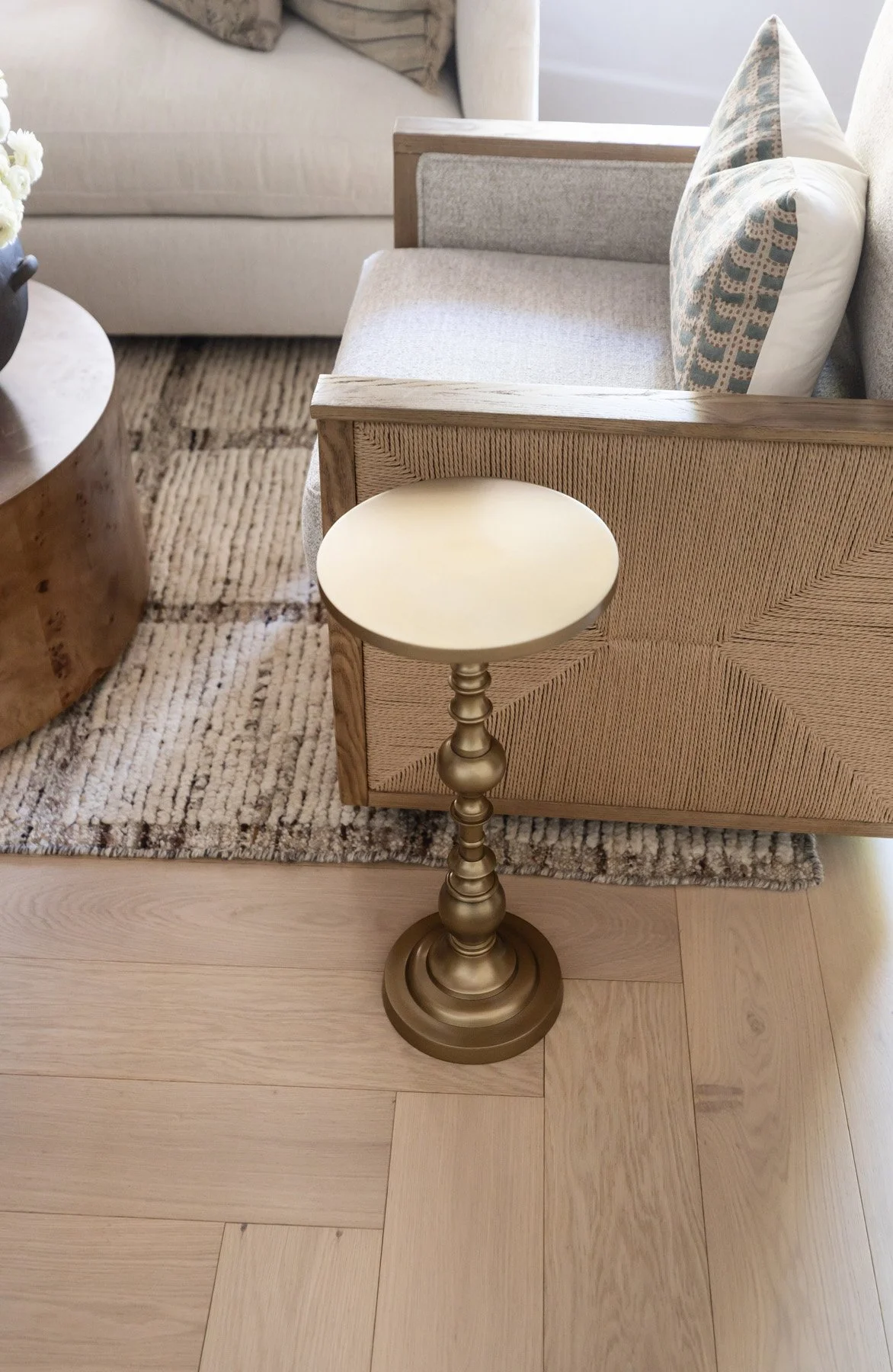Overhead detail of brass pedestal side table with on light oak herringbone floor, beside woven armchair