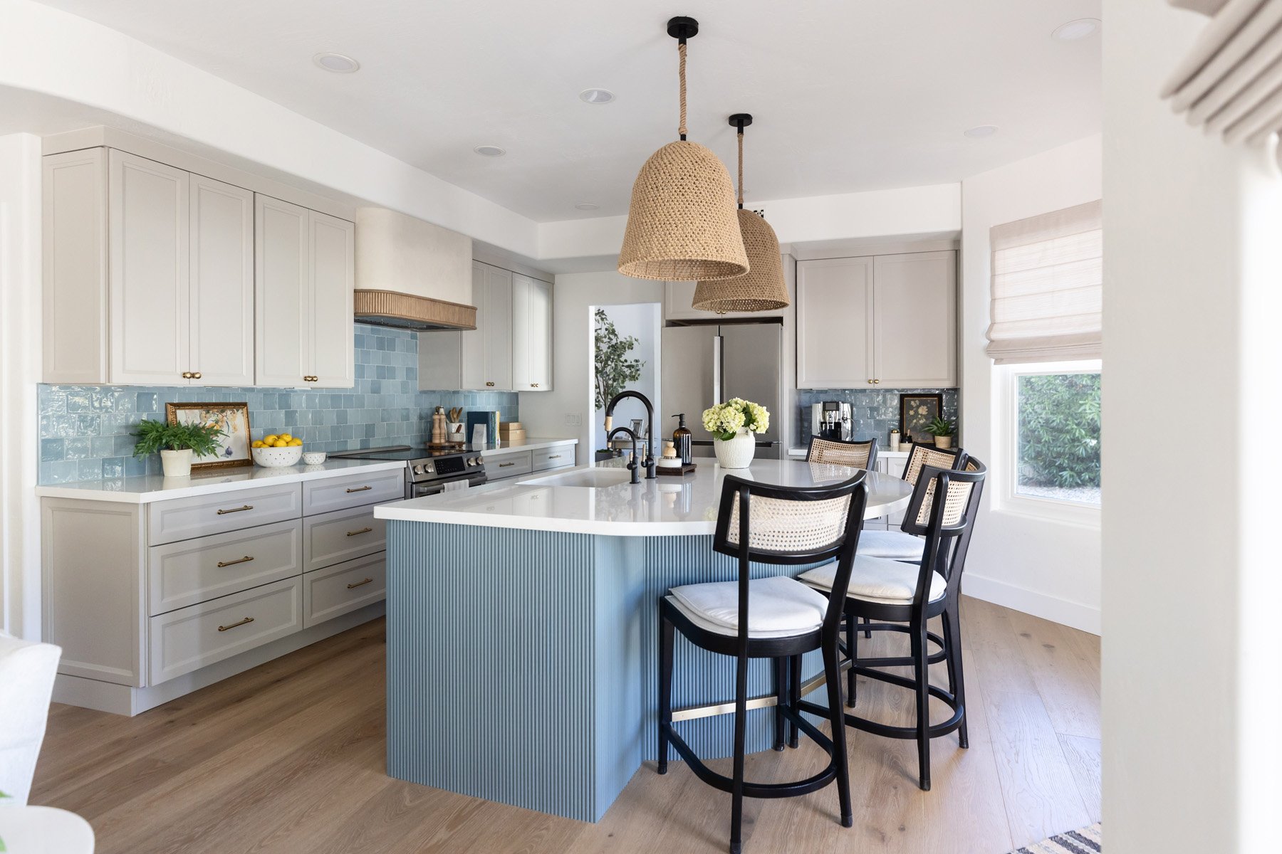 Scottsdale kitchen renovation with curved blue fluted island, white quartz countertop, black matte faucet, black cane bar stools, white shaker cabinetry with brass hardware, blue zellige tile backsplash, woven range hood, and woven pendant lights