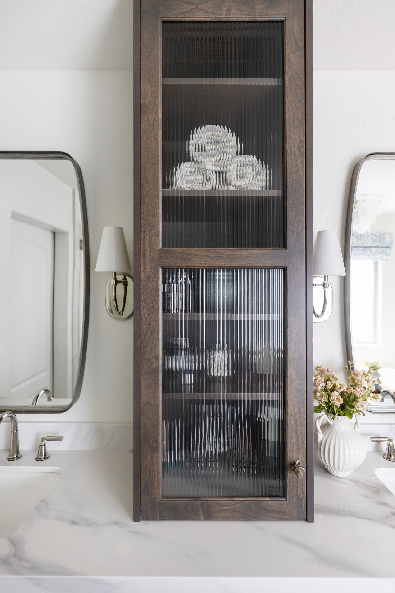 Dark wood vanity tower with reeded glass doors between two mirrors in a Phoenix bathroom