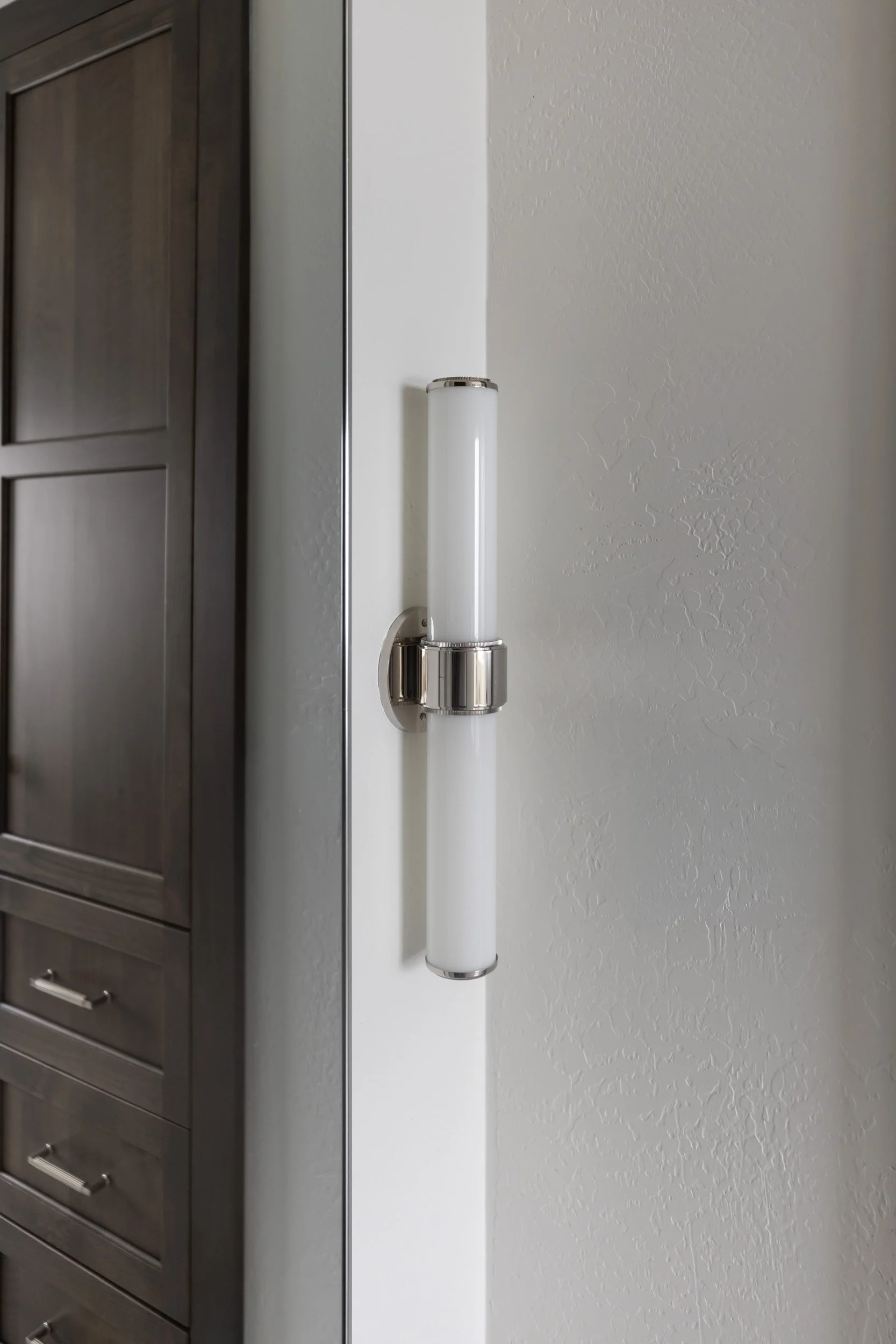 Linear wall sconce beside a dark wood bathroom cabinet in a Phoenix home