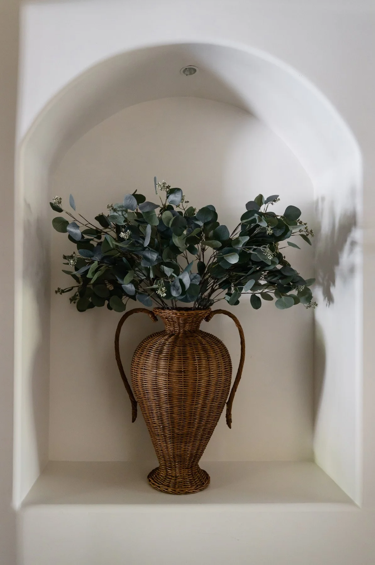 hite arched wall niche with large woven vase and eucalyptus arrangement