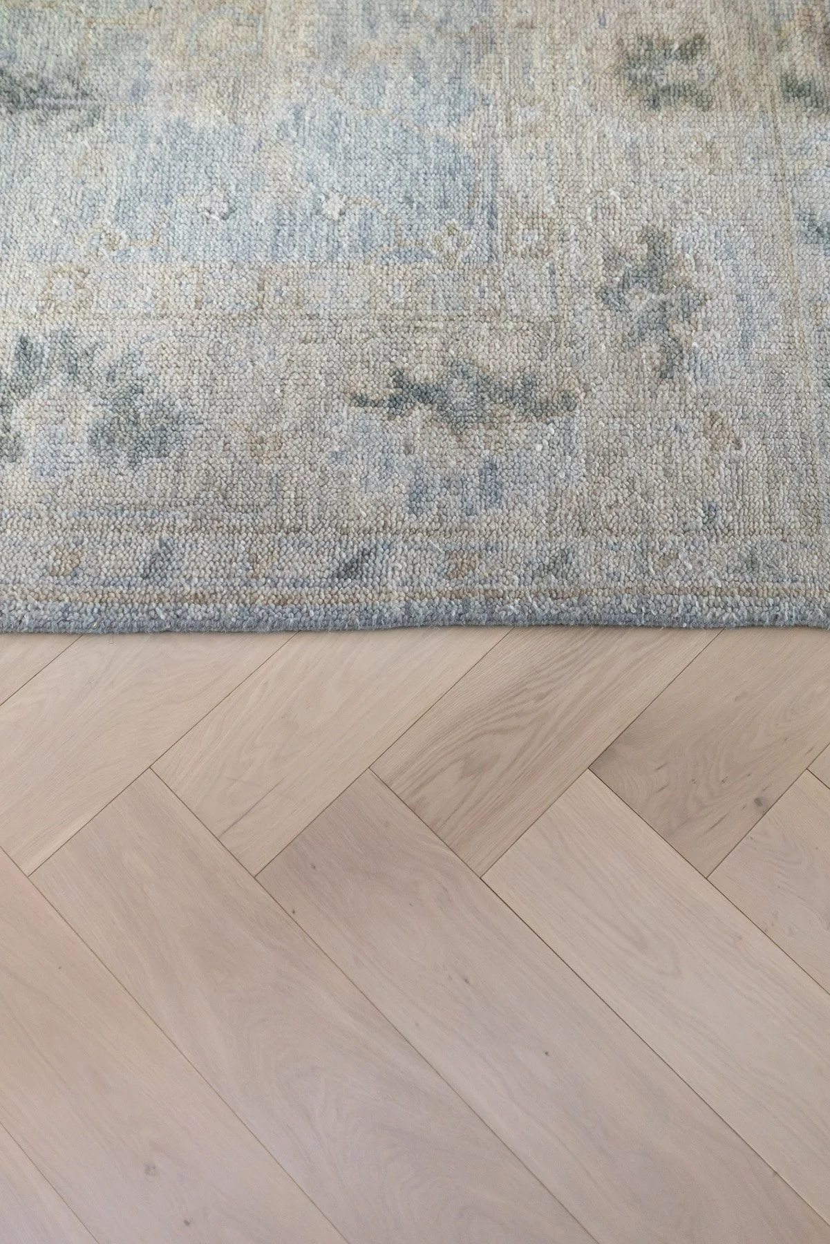 Close-up detail of light oak herringbone timber floor with vintage-style blue and grey rug edge