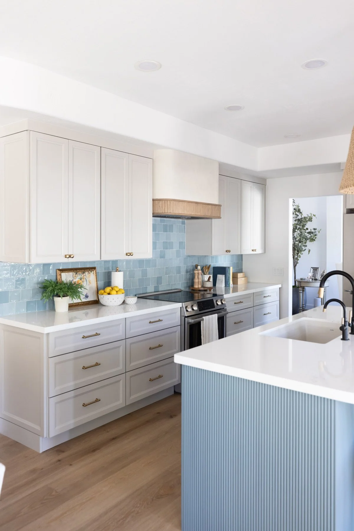 Kitchen with blue fluted island, white quartz countertop, white shaker cabinetry, blue zellige tile backsplash, black faucet, and stainless steel appliances
