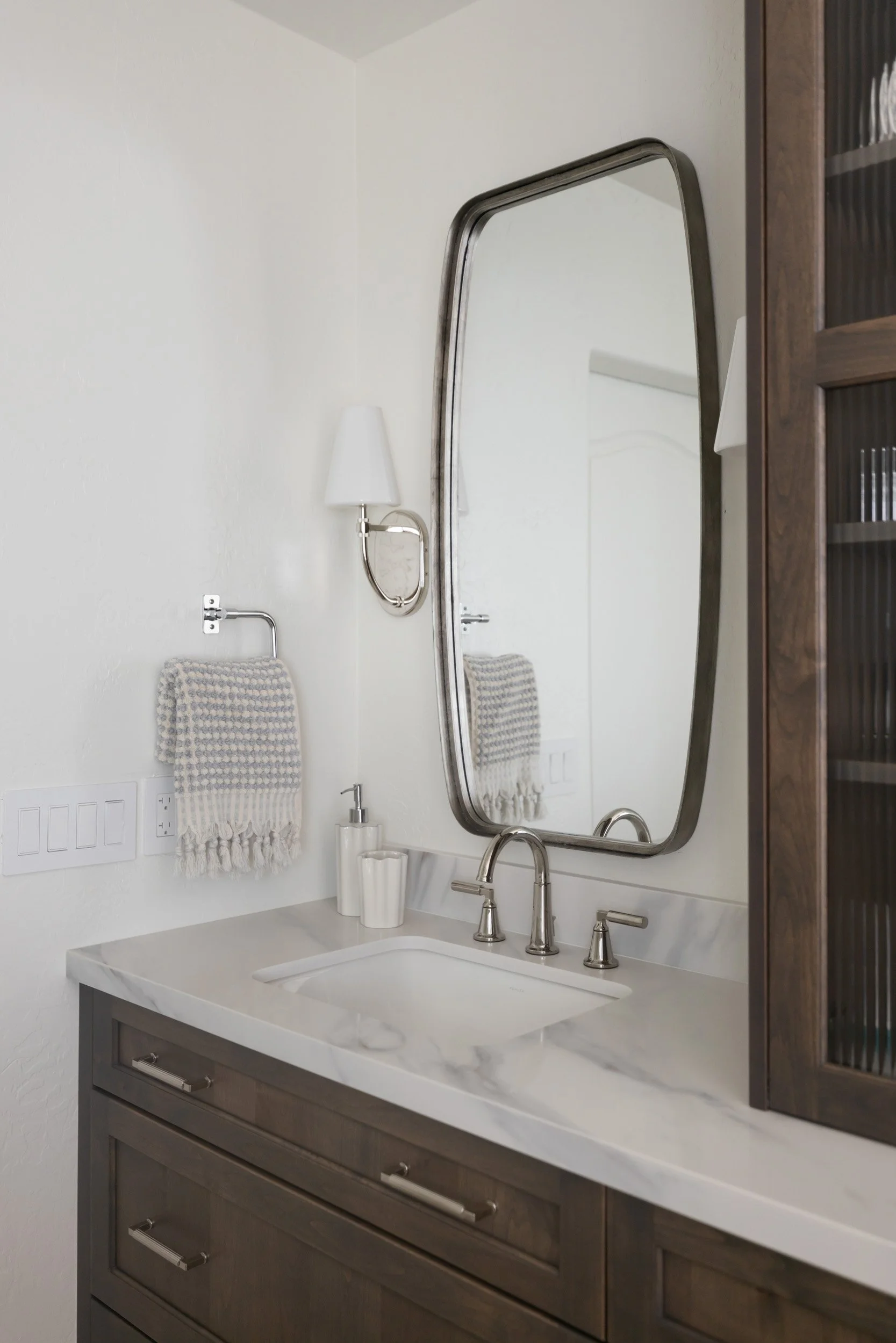 Rounded mirror, sconce and towel ring above a marble vanity in a Desert Ridge bathroom