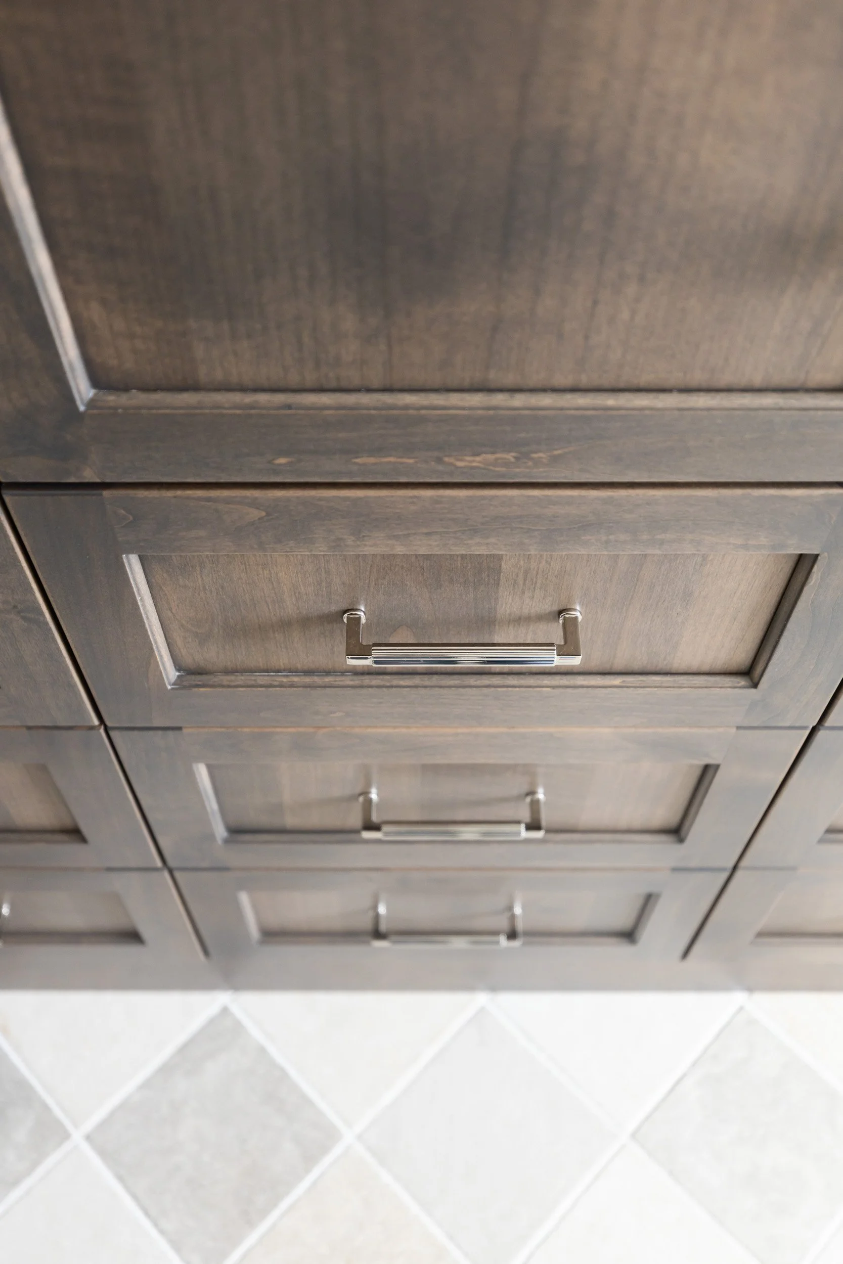 Dark wood vanity drawers with brushed nickel pulls above checkered tile, Desert Ridge