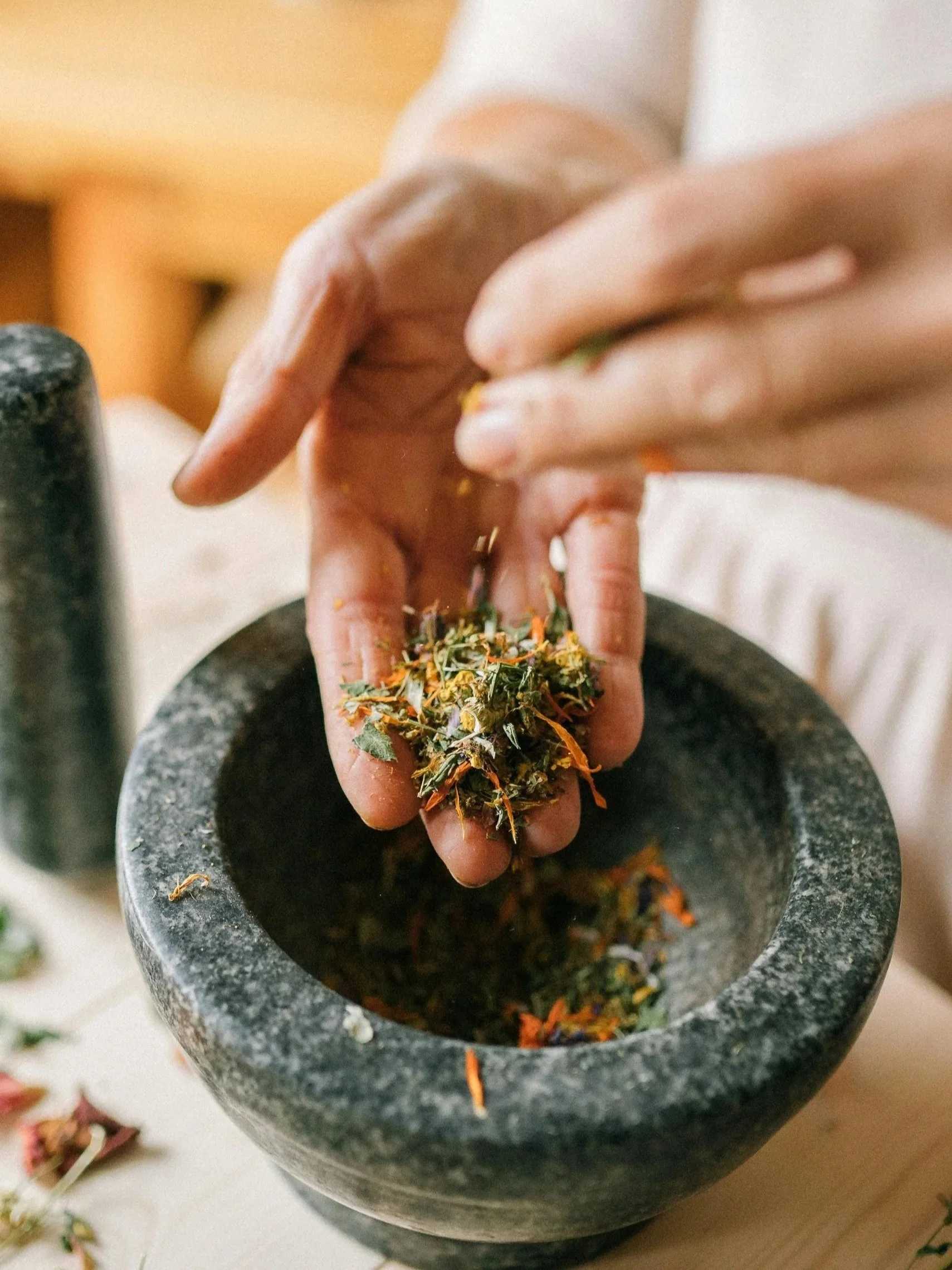 Person using a mortar and pestle to grind dried herbs and flowers.